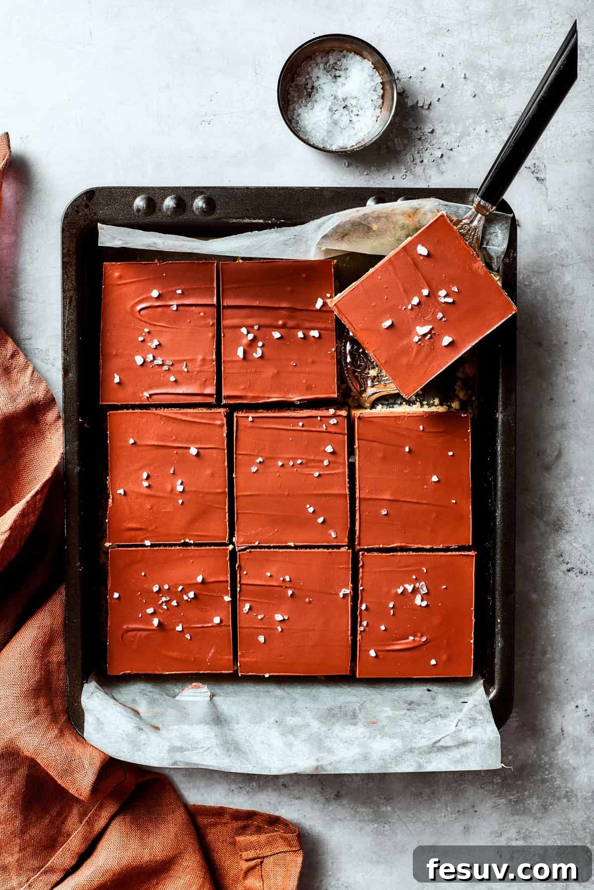 A serving utensil lifts out a square of millionaire bar from a pan.