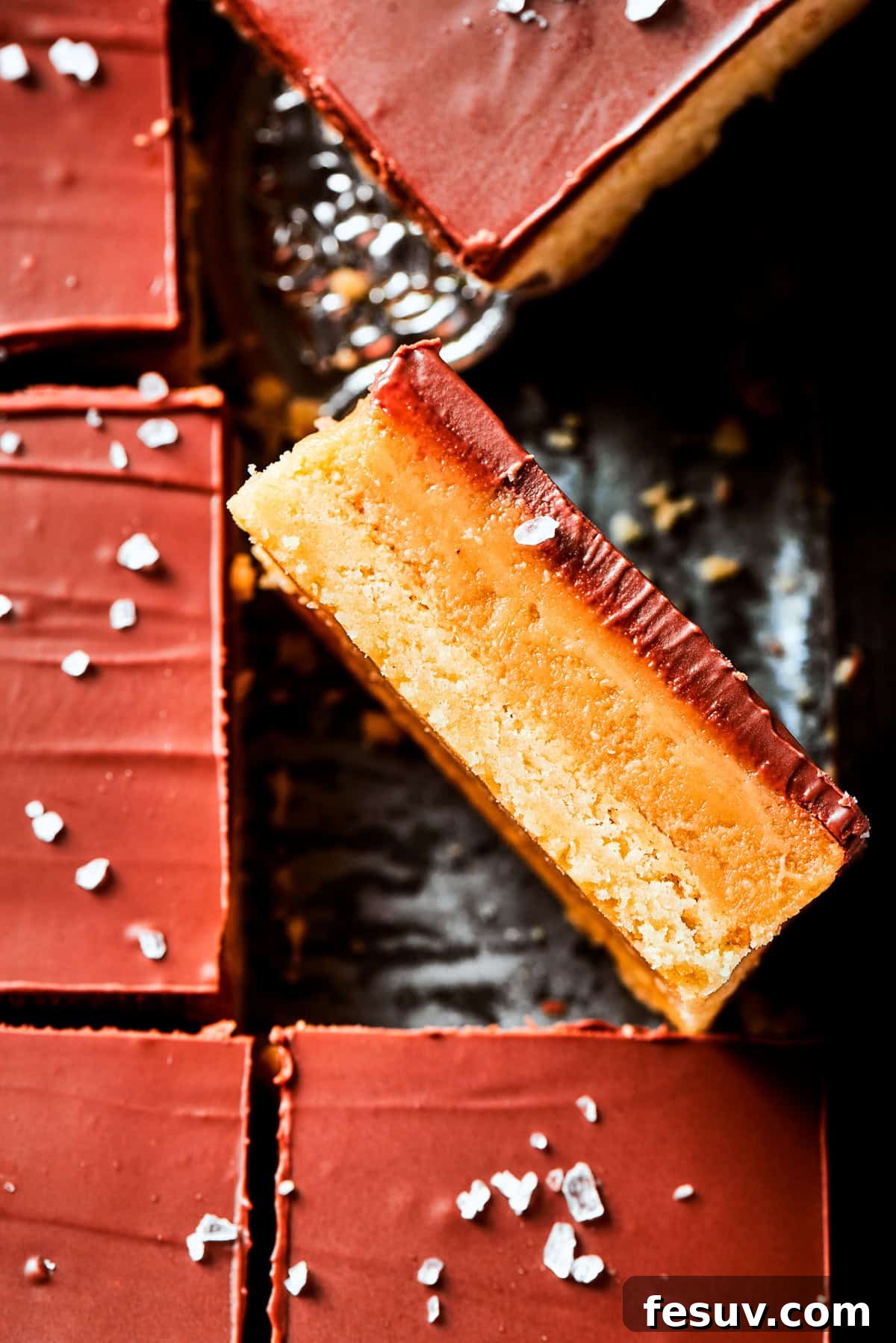 A millionaire bar turned on its side on top of a pan of finished millionaire bars, showing the distinct layers.