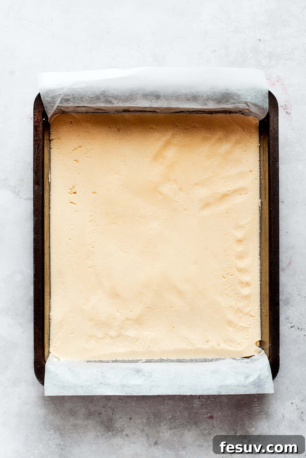 Shortbread dough is added to a parchment-lined baking pan and pressed down.
