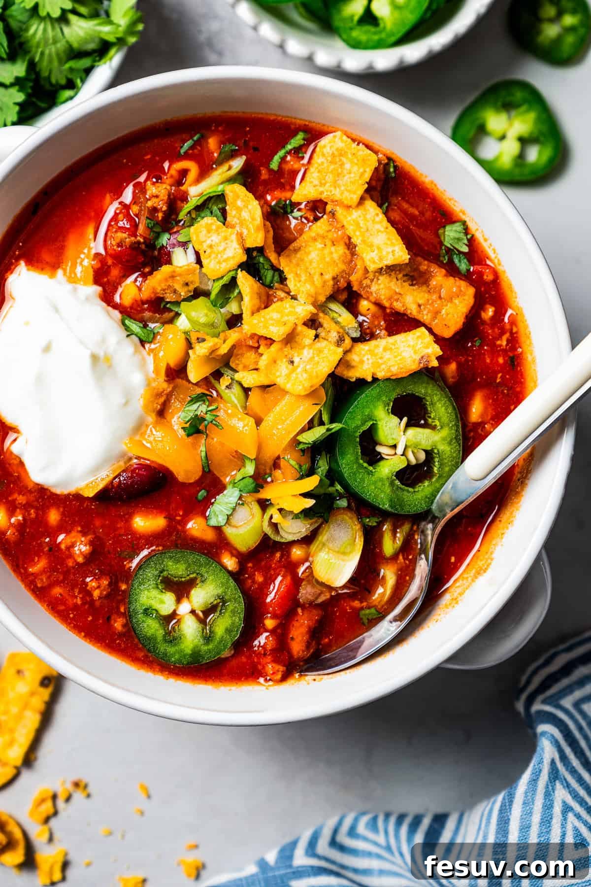 The BEST turkey chili recipe with juicy ground turkey, veggies, beans, and the perfect blend of spices. Great for weeknights and game days! Overhead image of a bowl of turkey chili garnished with sour cream, jalapeños, and corn chips, showcasing its rich texture and vibrant toppings.