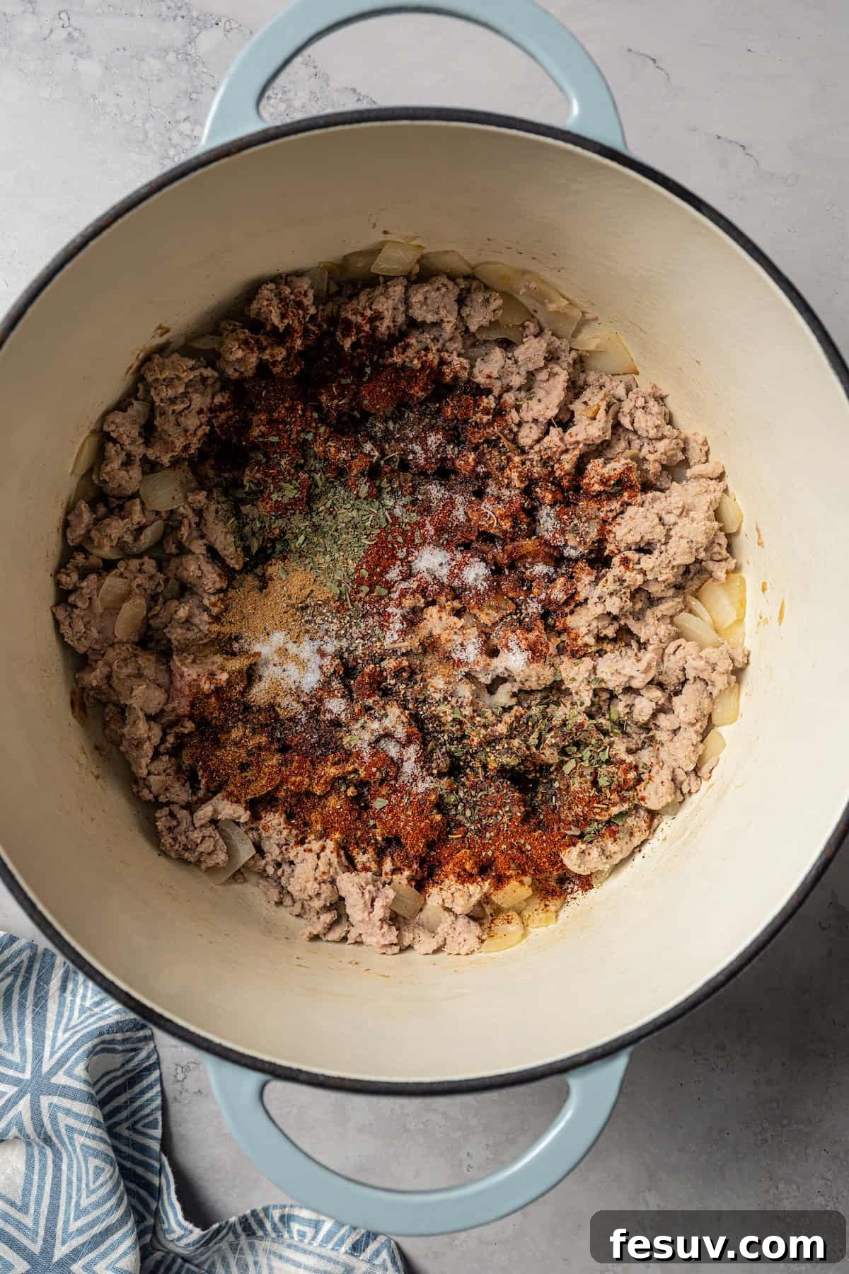 The BEST turkey chili recipe with juicy ground turkey, veggies, beans, and the perfect blend of spices. Great for weeknights and game days! Seasoning added to browned ground turkey and onions in a large pot, ready to be stirred for flavor infusion.