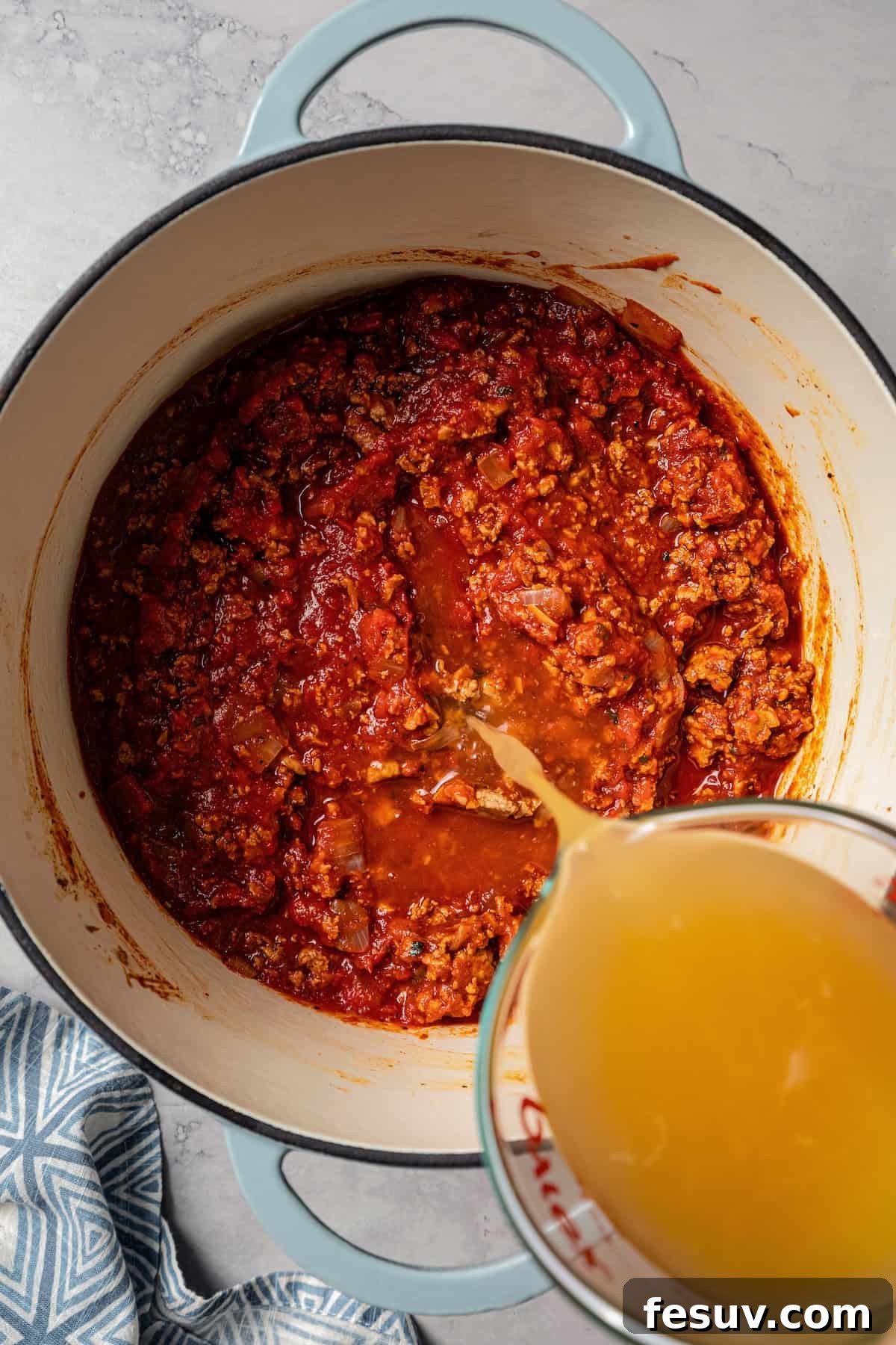 The BEST turkey chili recipe with juicy ground turkey, veggies, beans, and the perfect blend of spices. Great for weeknights and game days! Chicken broth being poured over the other turkey chili ingredients in a pot, ready for simmering.