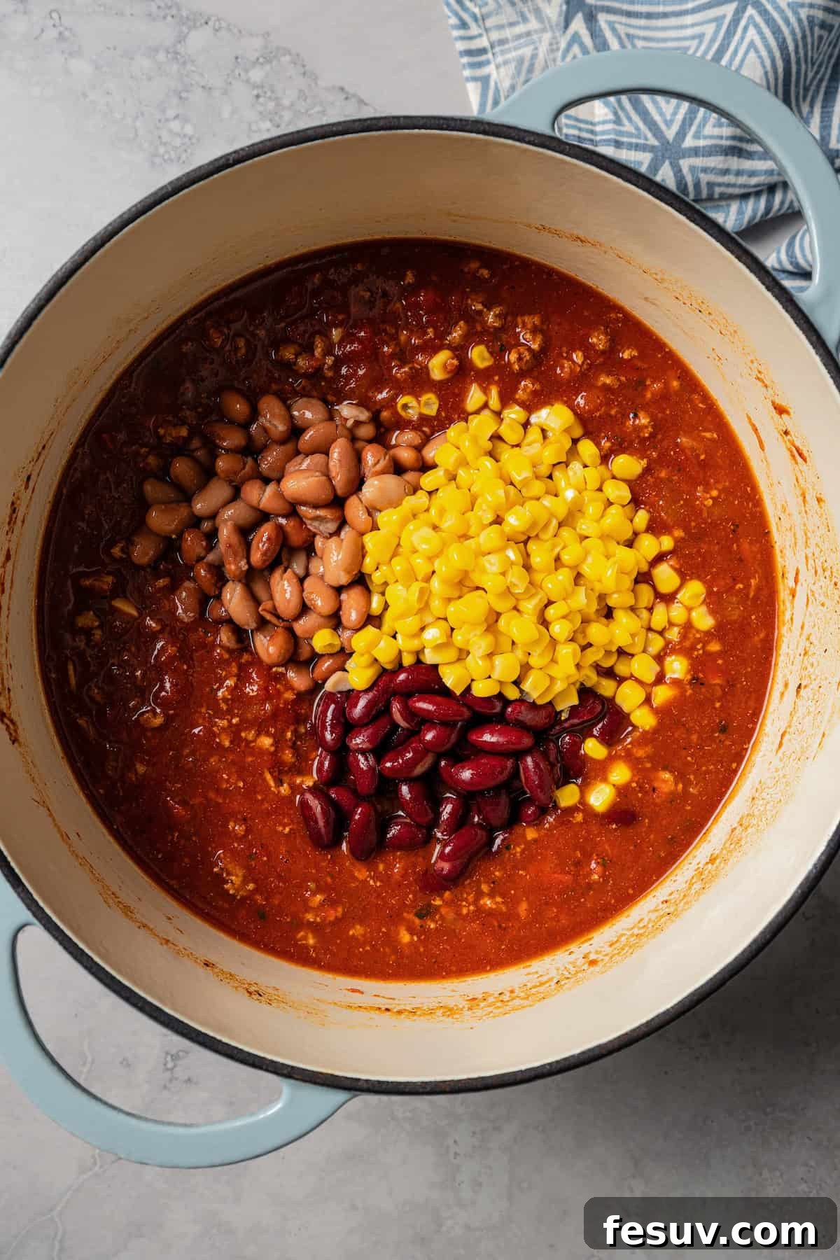 The BEST turkey chili recipe with juicy ground turkey, veggies, beans, and the perfect blend of spices. Great for weeknights and game days! Canned corn and beans added to a pot with turkey chili, enhancing texture and nutritional value.