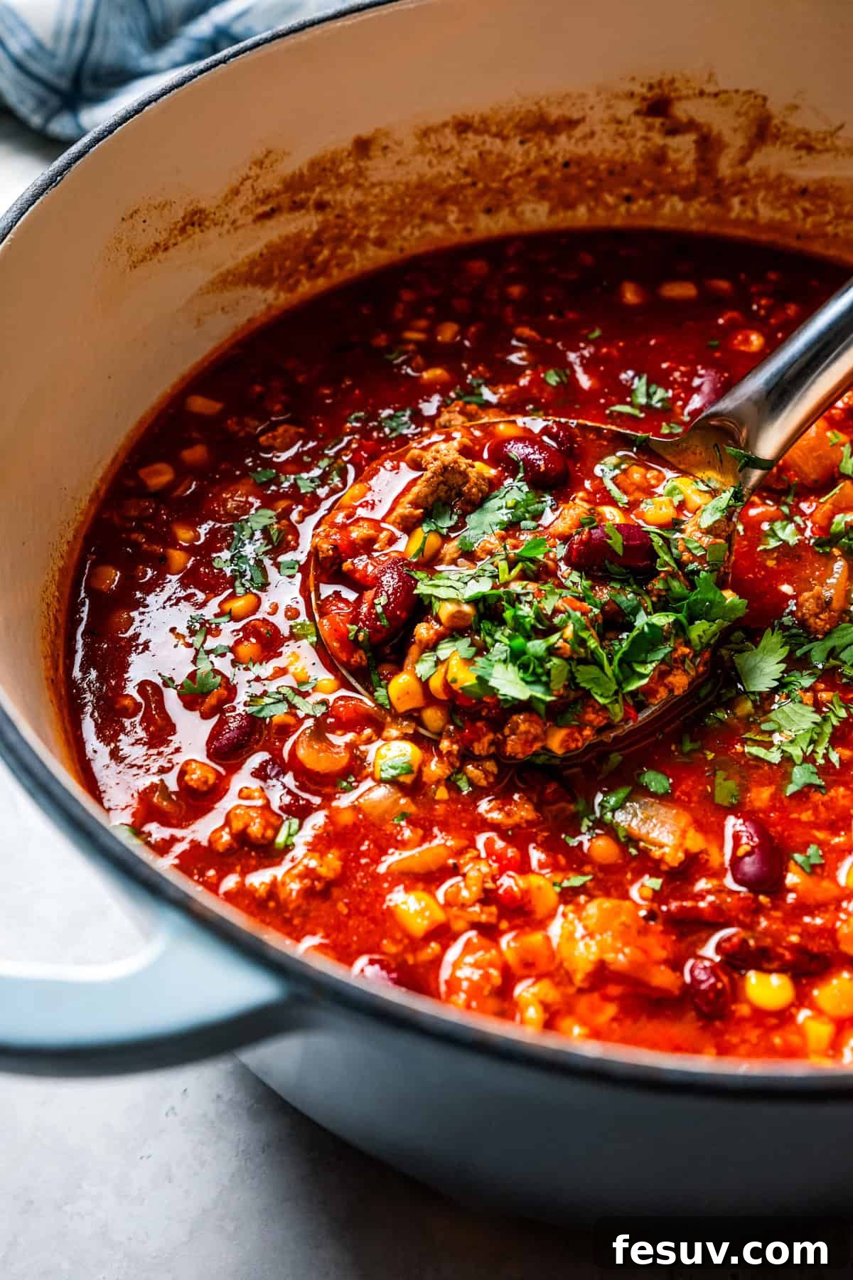 The BEST turkey chili recipe with juicy ground turkey, veggies, beans, and the perfect blend of spices. Great for weeknights and game days! A close-up of a ladle scooping rich turkey chili from a large, steaming Dutch oven, showing its thick, hearty texture.