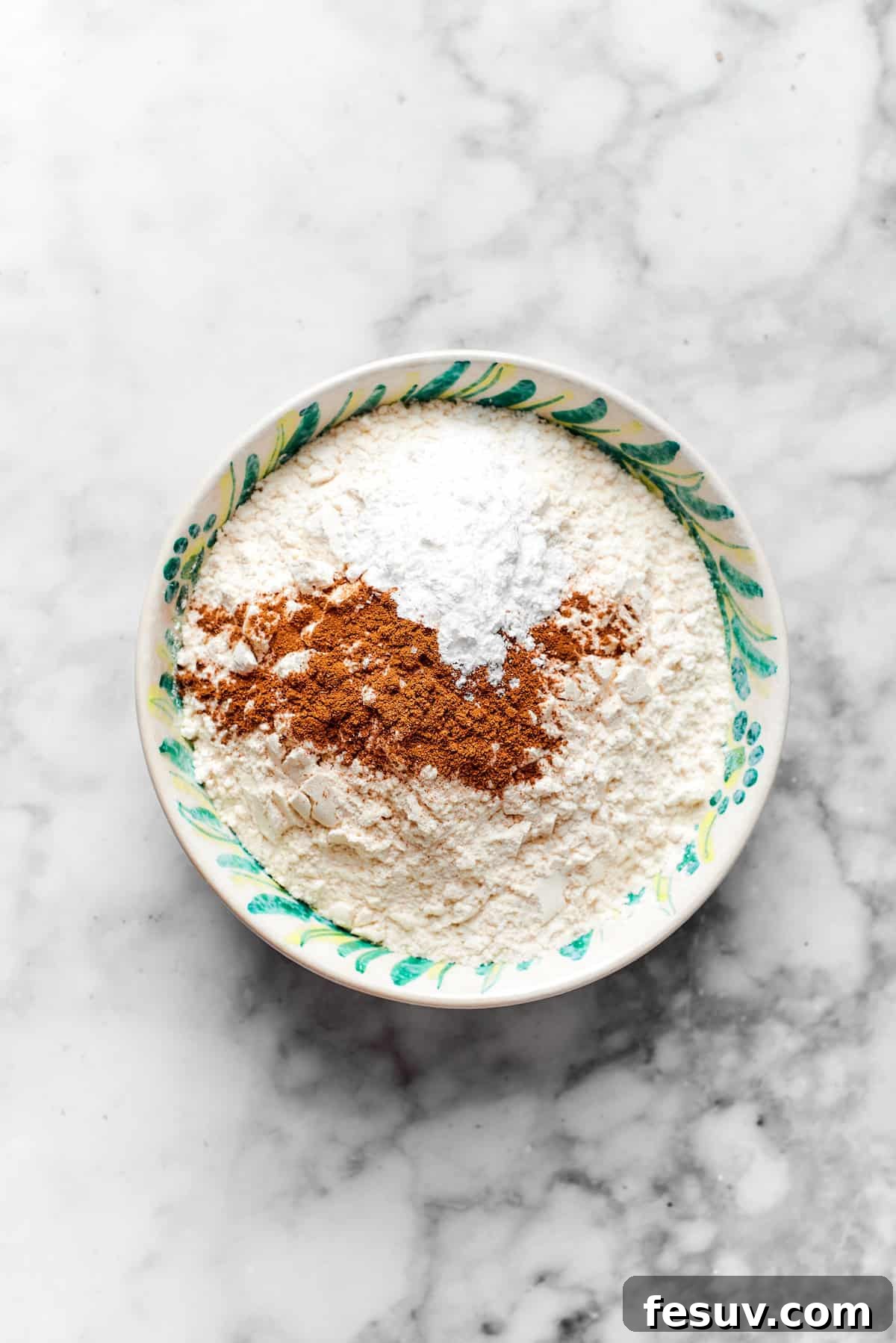 Spices and baking powder are mixed with flour in a bowl.
