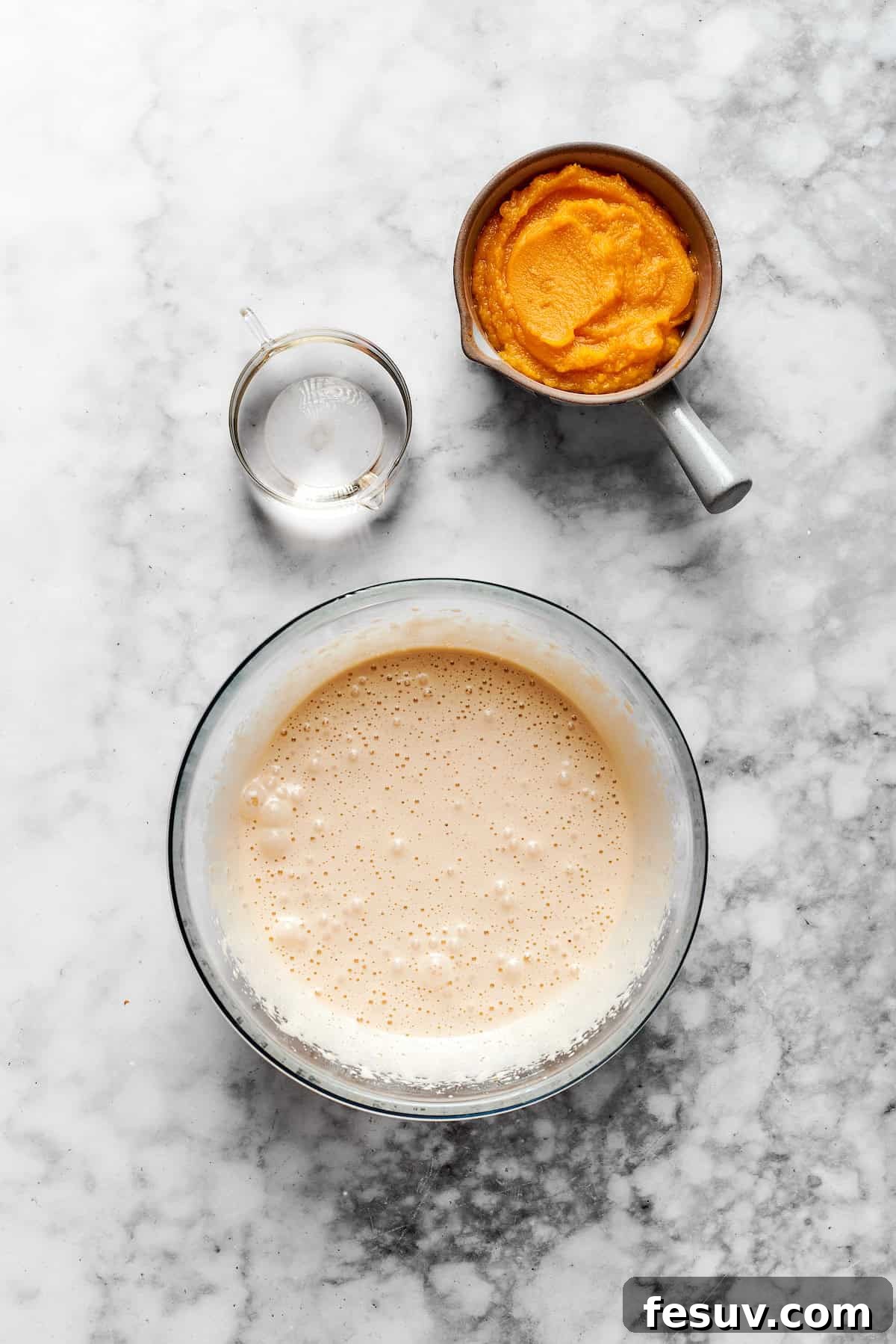 A bowl of muffin batter with a cup of pumpkin puree.