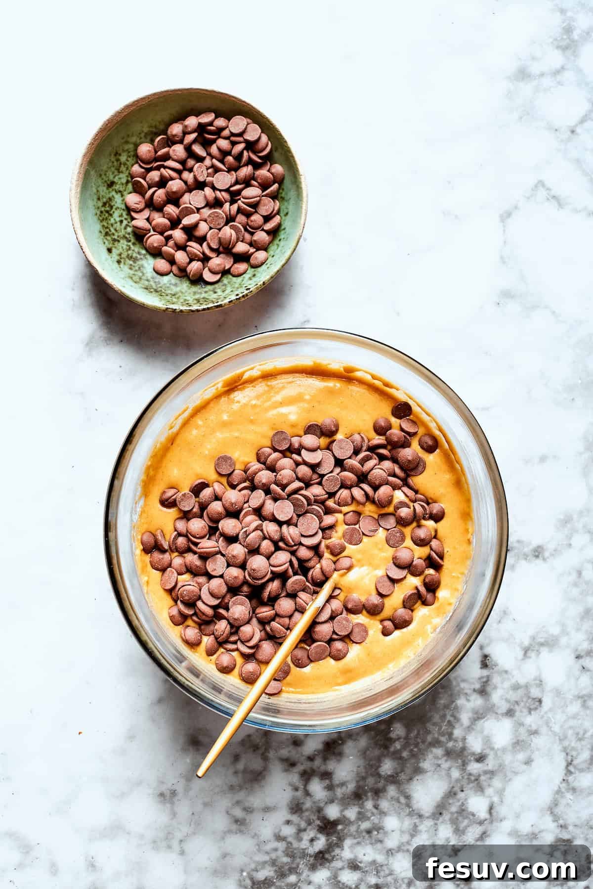 Chocolate chips are added to a bowl of pumpkin muffin batter.