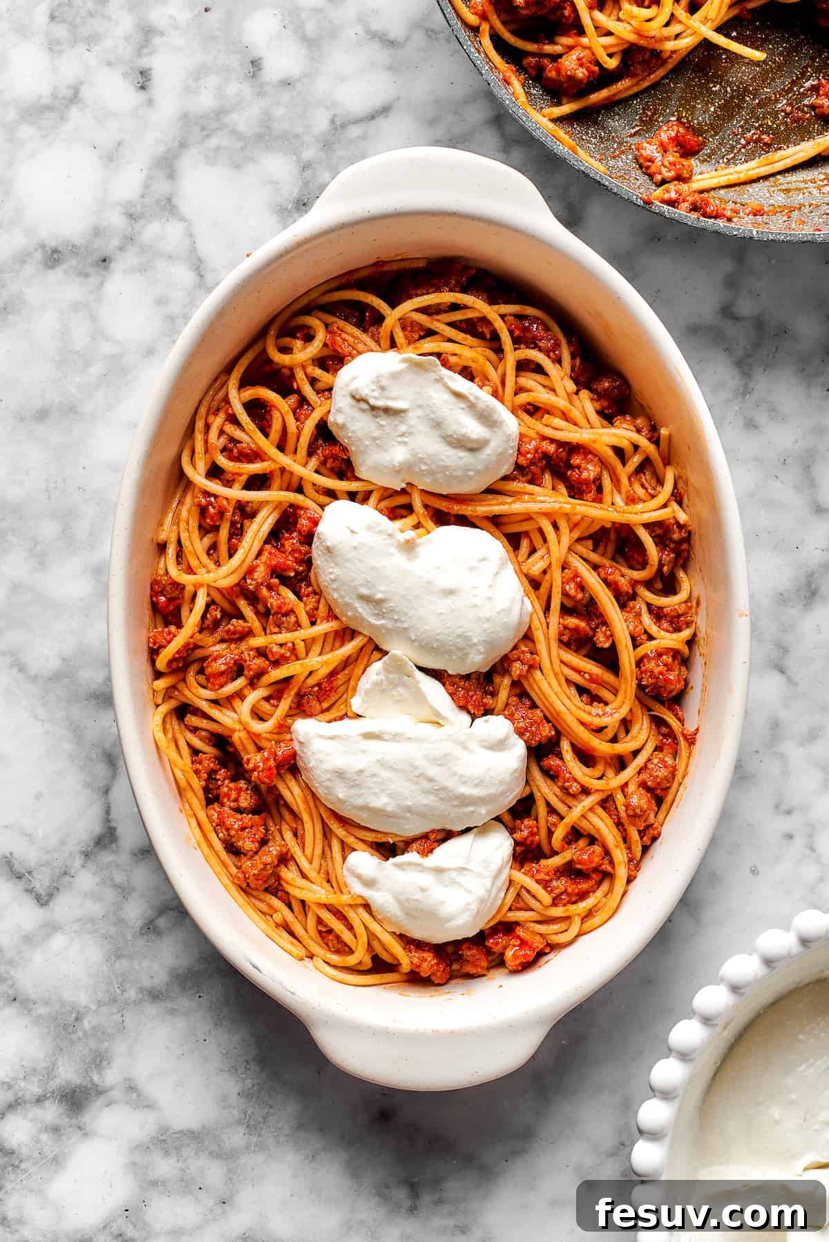 Layering Cheese and Pasta in the Casserole Spreading the creamy cheese mixture over a layer of spaghetti and meat sauce in a baking dish.