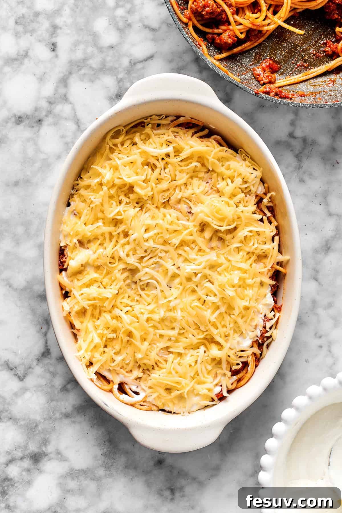 Final Cheese Topping Before Baking A final layer of shredded mozzarella and Parmesan cheese topping the spaghetti casserole in a 9x13 inch dish, ready for baking.