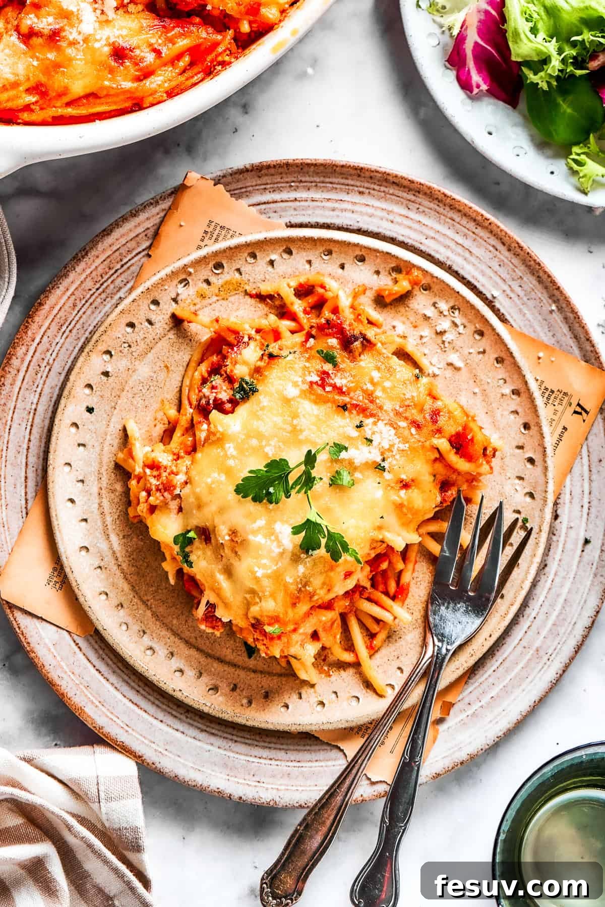 A Delicious Serving of Million Dollar Spaghetti A perfectly portioned serving of Million Dollar Spaghetti on a white plate, accompanied by forks, showcasing its layers.