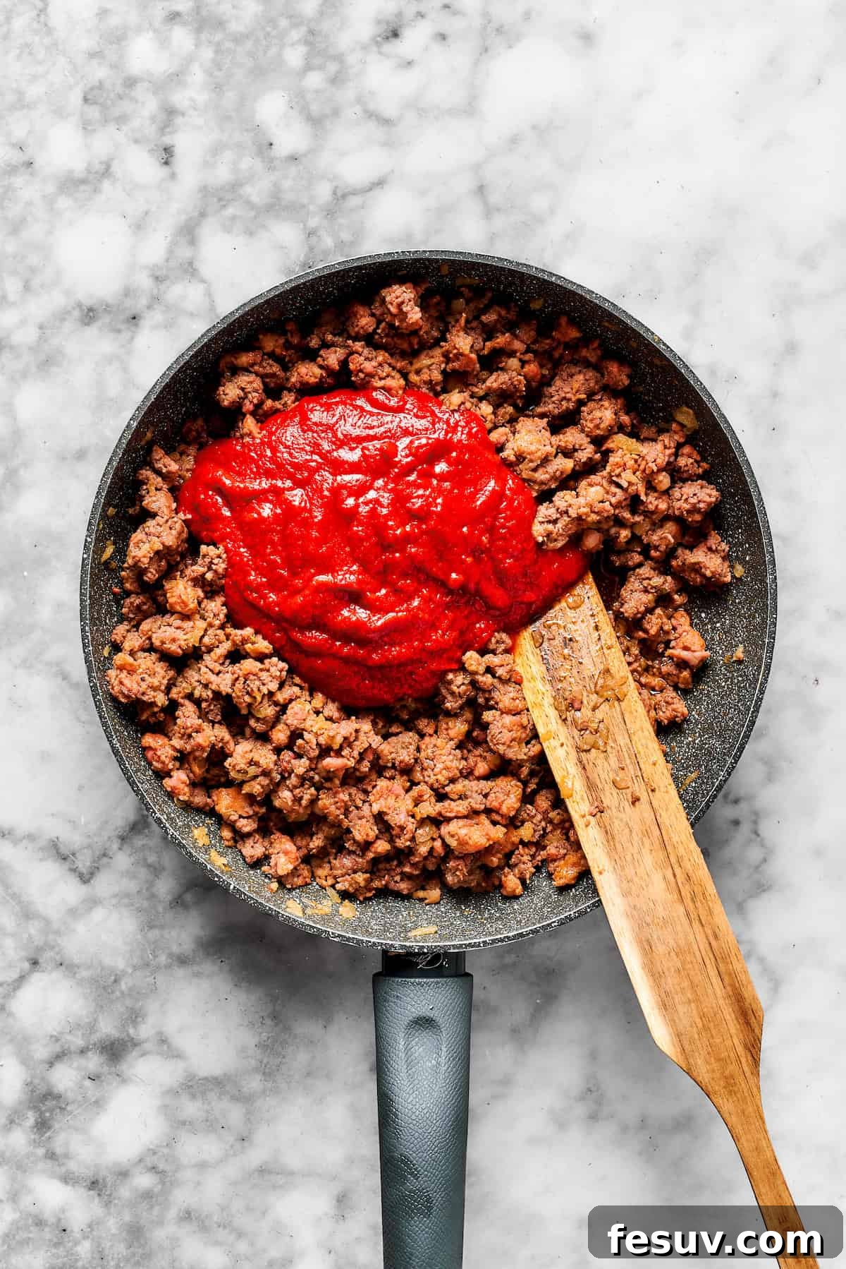 Combining Meat with Marinara Sauce Pouring marinara sauce into a skillet containing the browned and seasoned meat mixture.