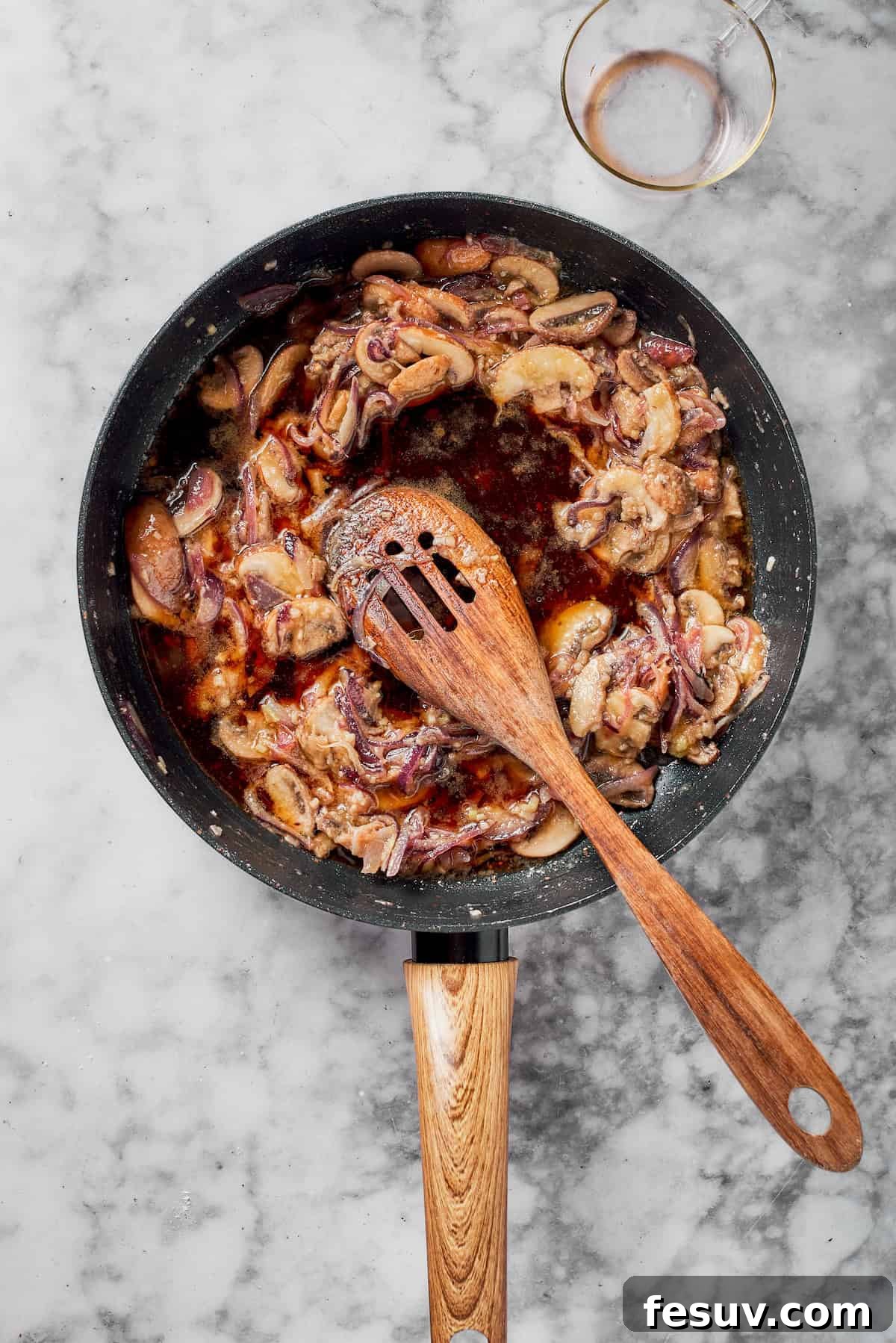 Pouring Marsala wine into a skillet with sautéed mushrooms and onions, after flour has been stirred in.