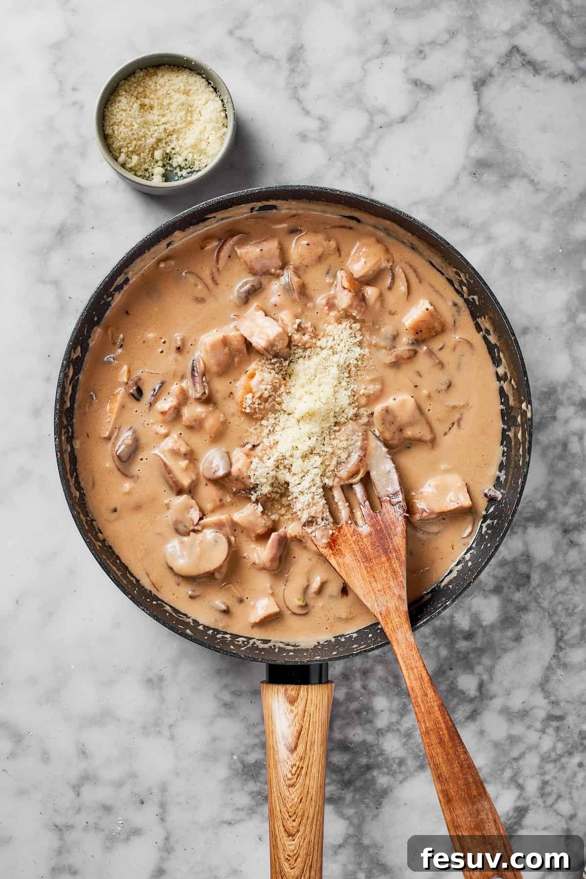 Chopped cooked chicken and freshly grated Parmesan cheese being added to the simmering Marsala sauce in a skillet.