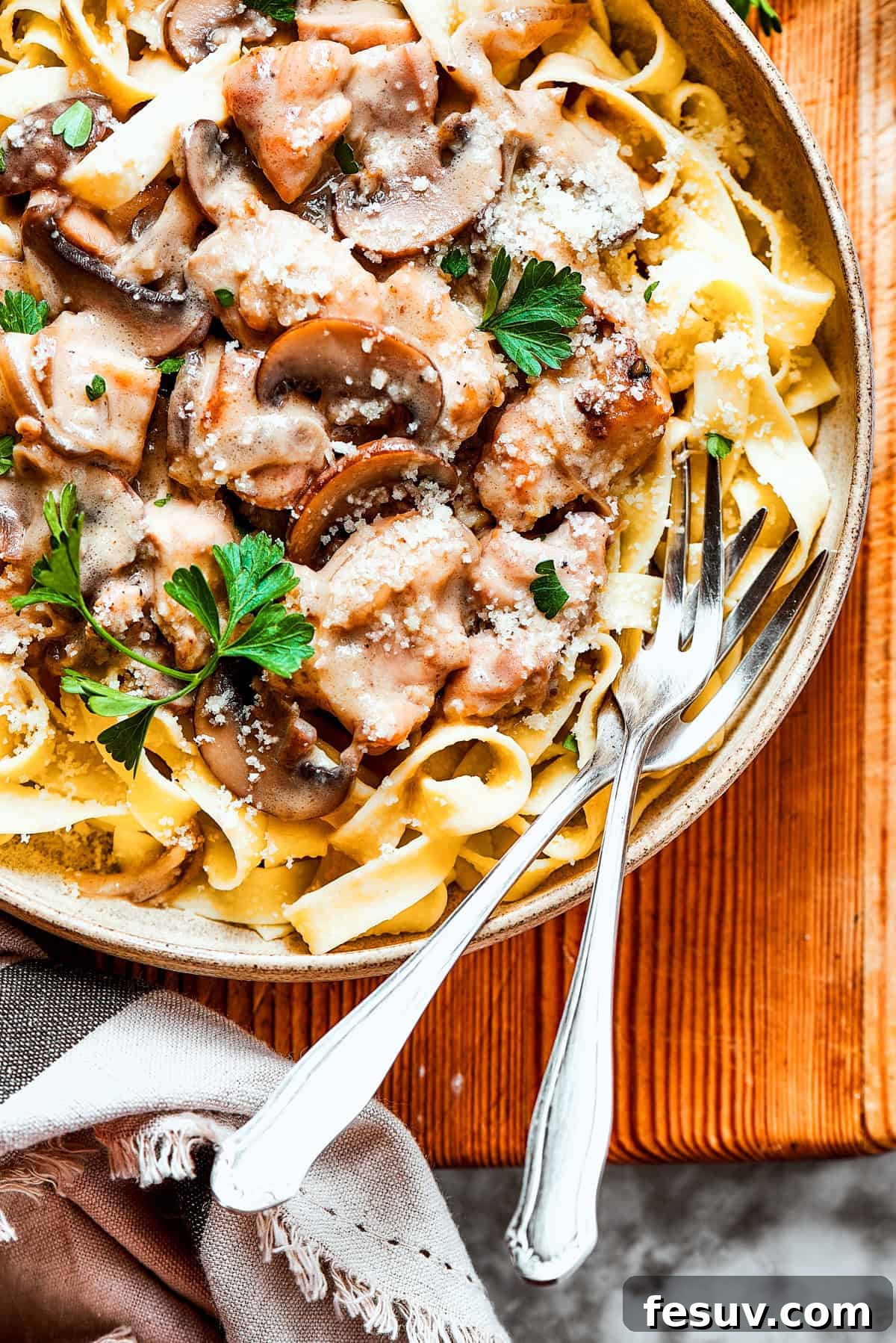 A beautifully composed bowl of creamy Chicken Marsala Fettuccine, with two elegant forks resting within the noodles, ready to be enjoyed. The dish showcases tender chicken, mushrooms, and a rich, golden sauce.