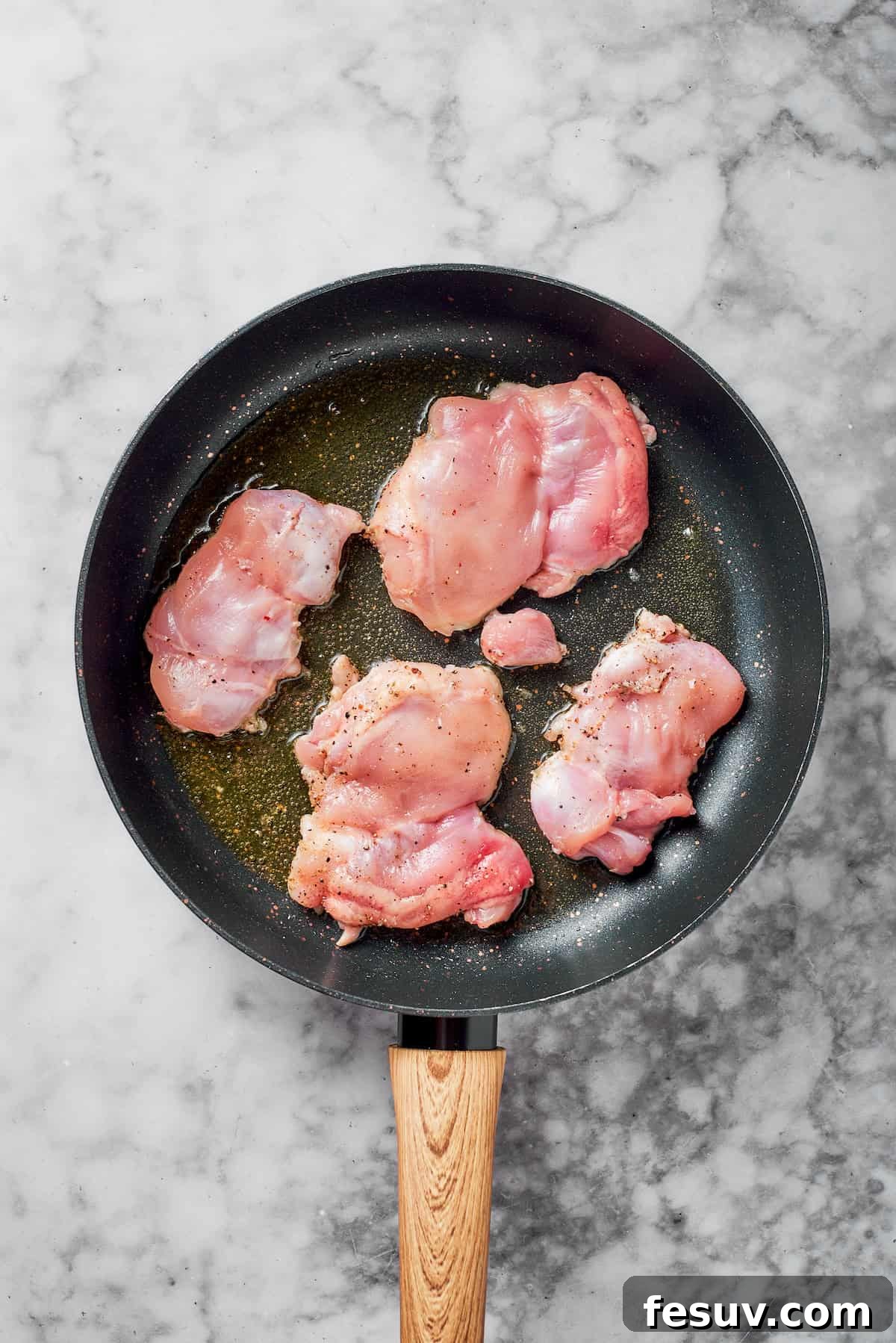 Boneless chicken thighs sizzling and browning in a hot skillet with olive oil.