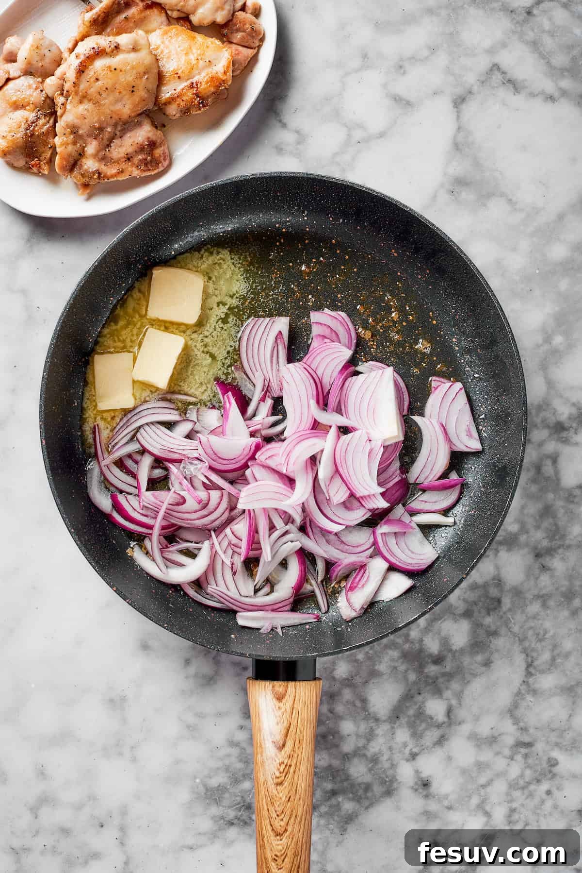 Thinly sliced red onions caramelizing in melted butter within a skillet.