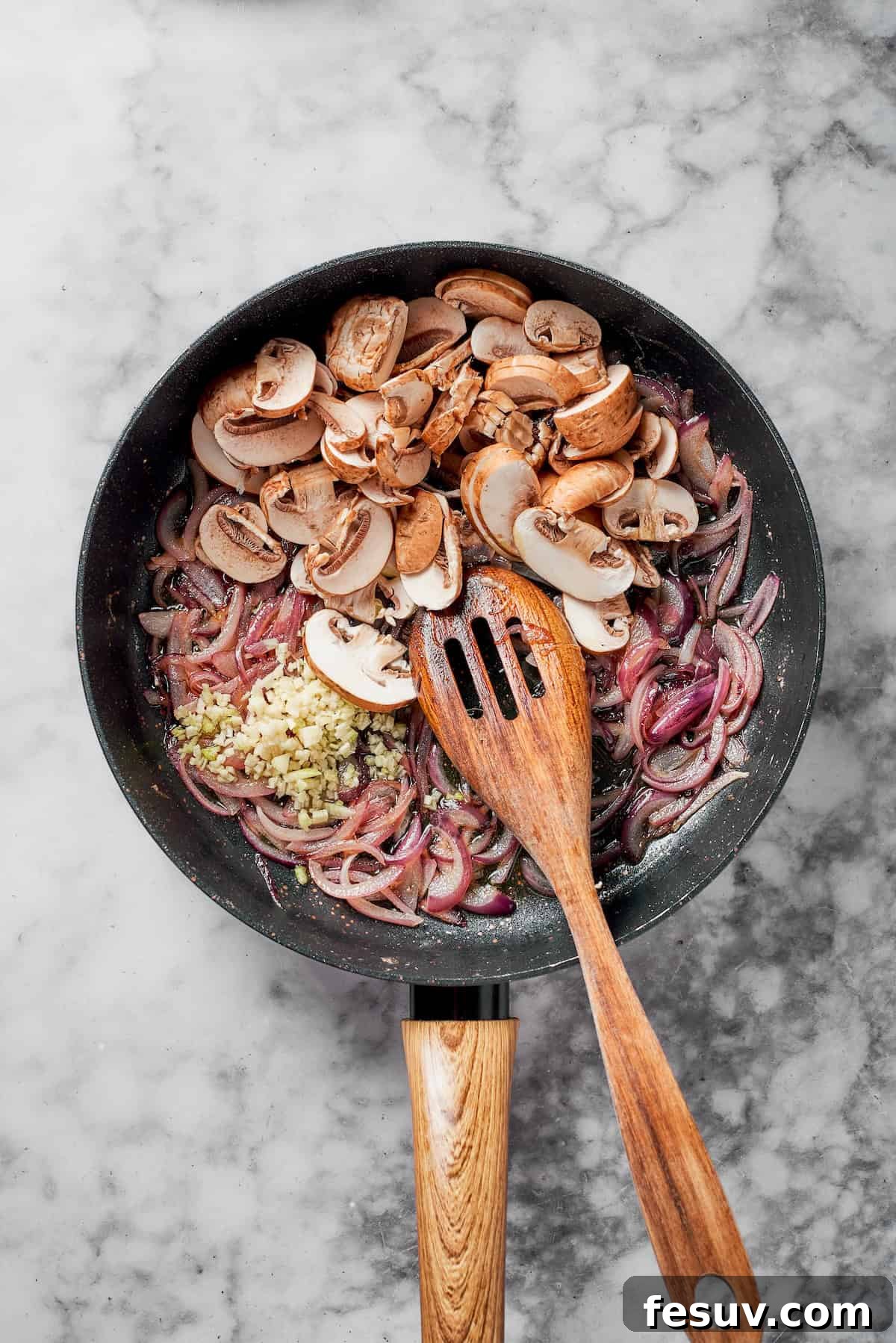 Sliced cremini mushrooms and minced garlic added to caramelized onions in a pan.