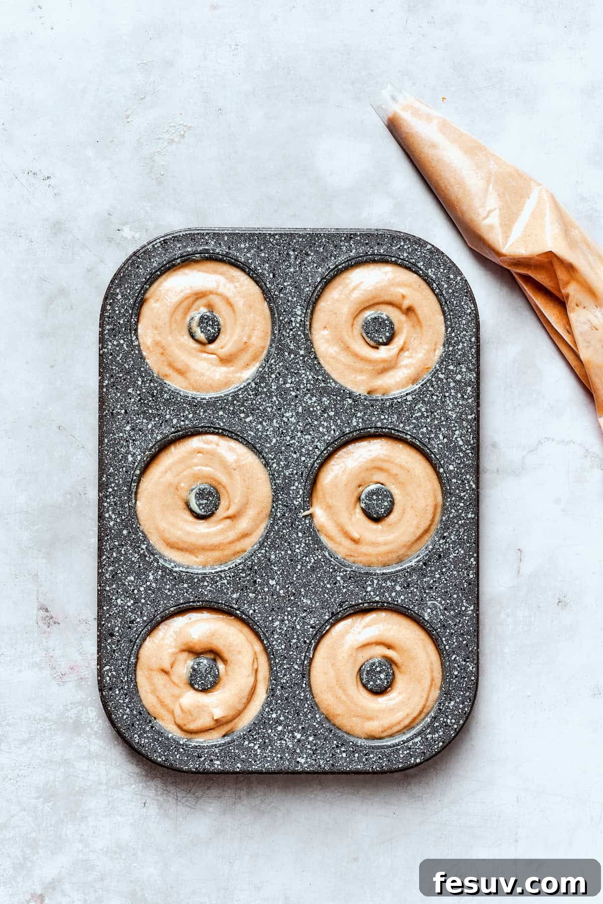 A donut pan with batter neatly piped into each well, ready for baking.