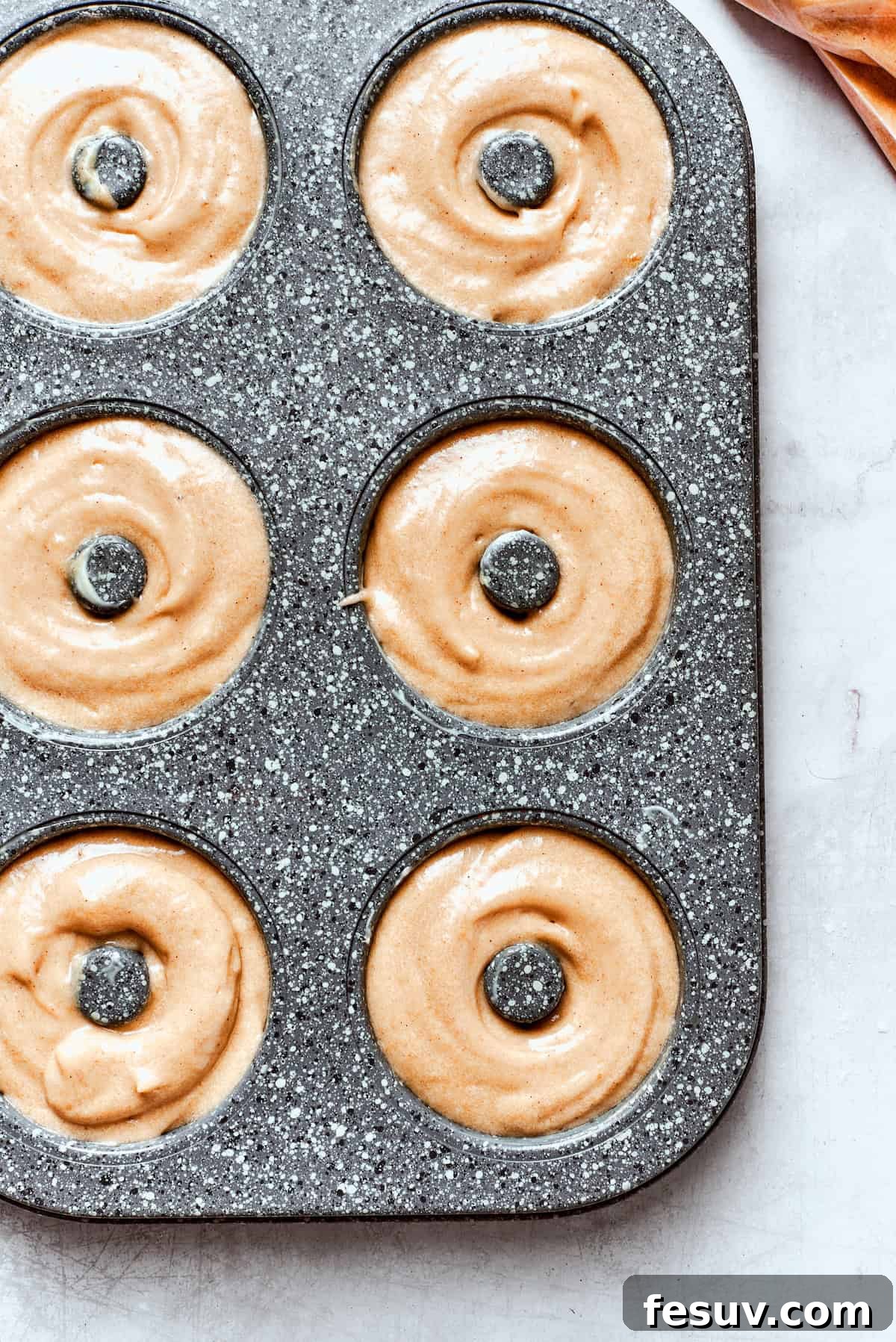 A top-down view of a donut pan, each cavity perfectly filled with smooth apple cider donut batter, showcasing its readiness for the oven.