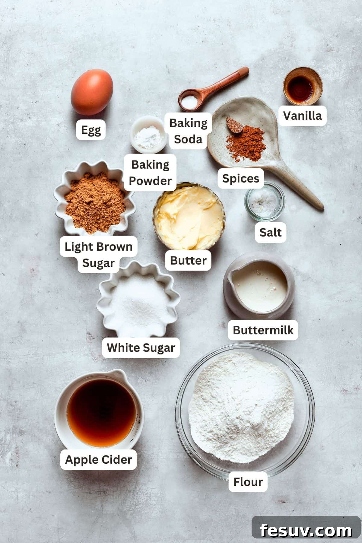 A vibrant flat lay of all ingredients for baked apple cider donuts, including fresh apple cider, butter, sugars, flour, and a selection of warm fall spices like cinnamon, nutmeg, and allspice.