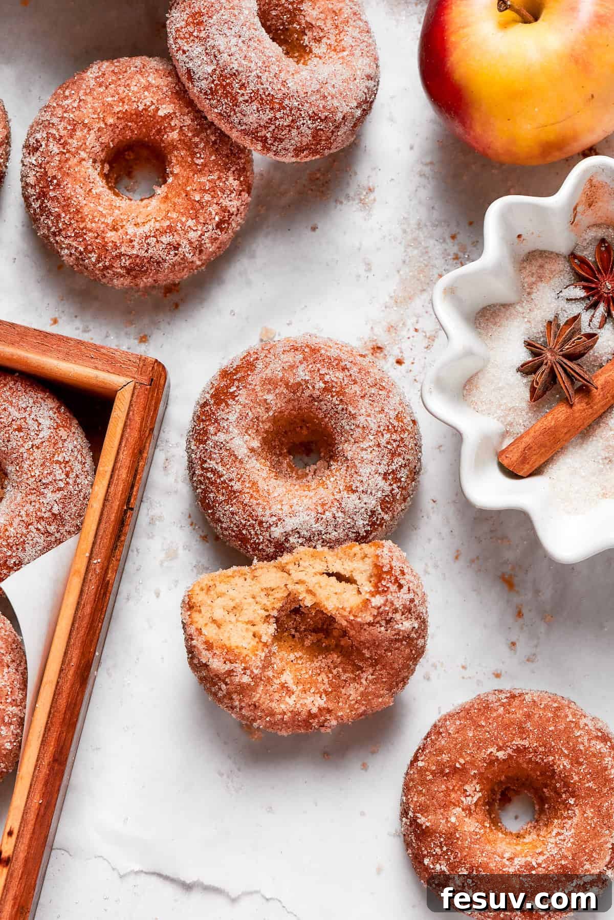 A close-up of a stack of baked apple cider donuts, with one donut having a bite taken out, revealing its soft, moist interior and spiced sugar coating.