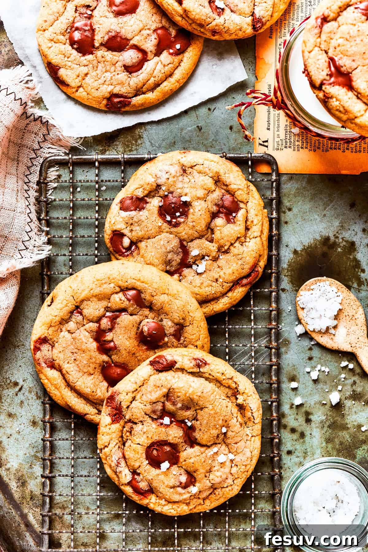 Three golden brown butter chocolate chip cookies on a cooling rack, glistening with melted chocolate.