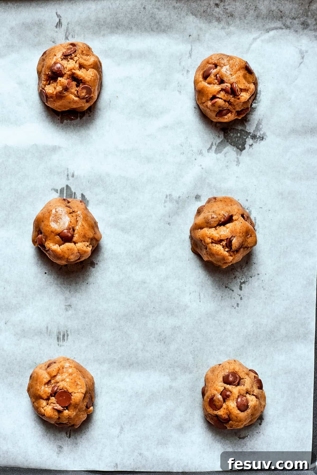 Uniform balls of brown butter chocolate chip cookie dough arranged on a parchment-lined baking sheet, spaced for baking.