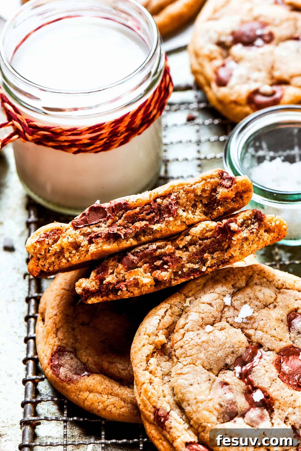Warm brown butter chocolate chip cookies resting on a wire rack next to a vintage jug of fresh milk.