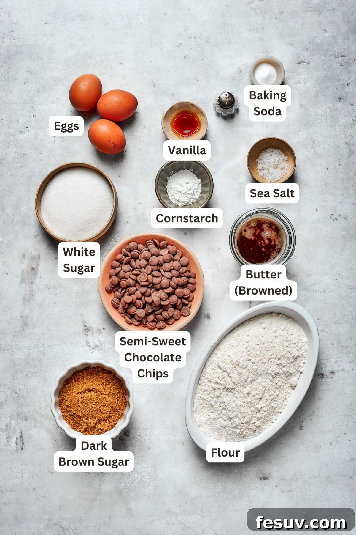 A selection of high-quality ingredients for brown butter chocolate chip cookies, including unsalted butter, granulated sugar, dark brown sugar, eggs, vanilla extract, all-purpose flour, cornstarch, baking soda, salt, semi-sweet chocolate chips, and flaky sea salt.
