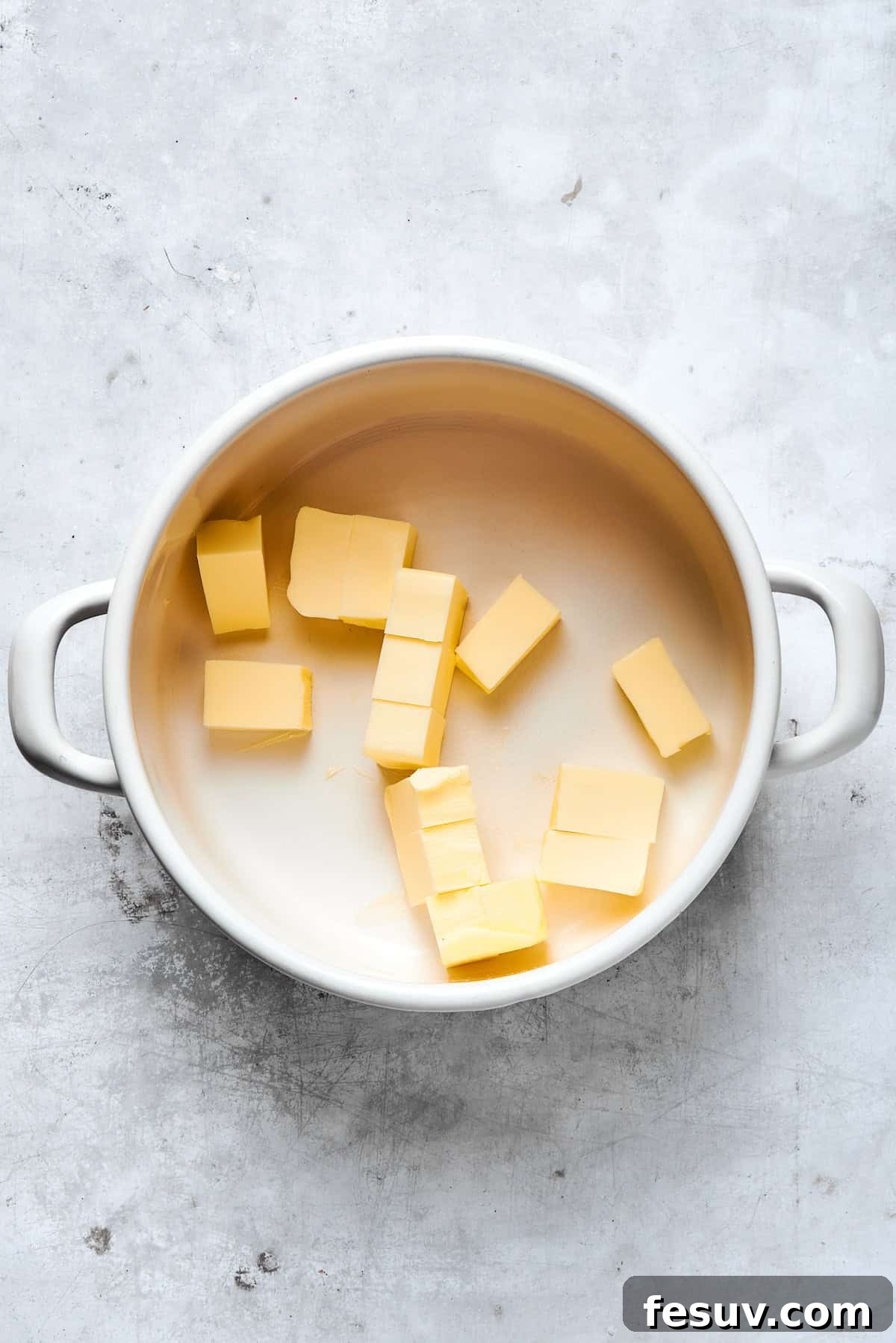 Unsalted butter cubes beginning to melt in a saucepan over medium heat.