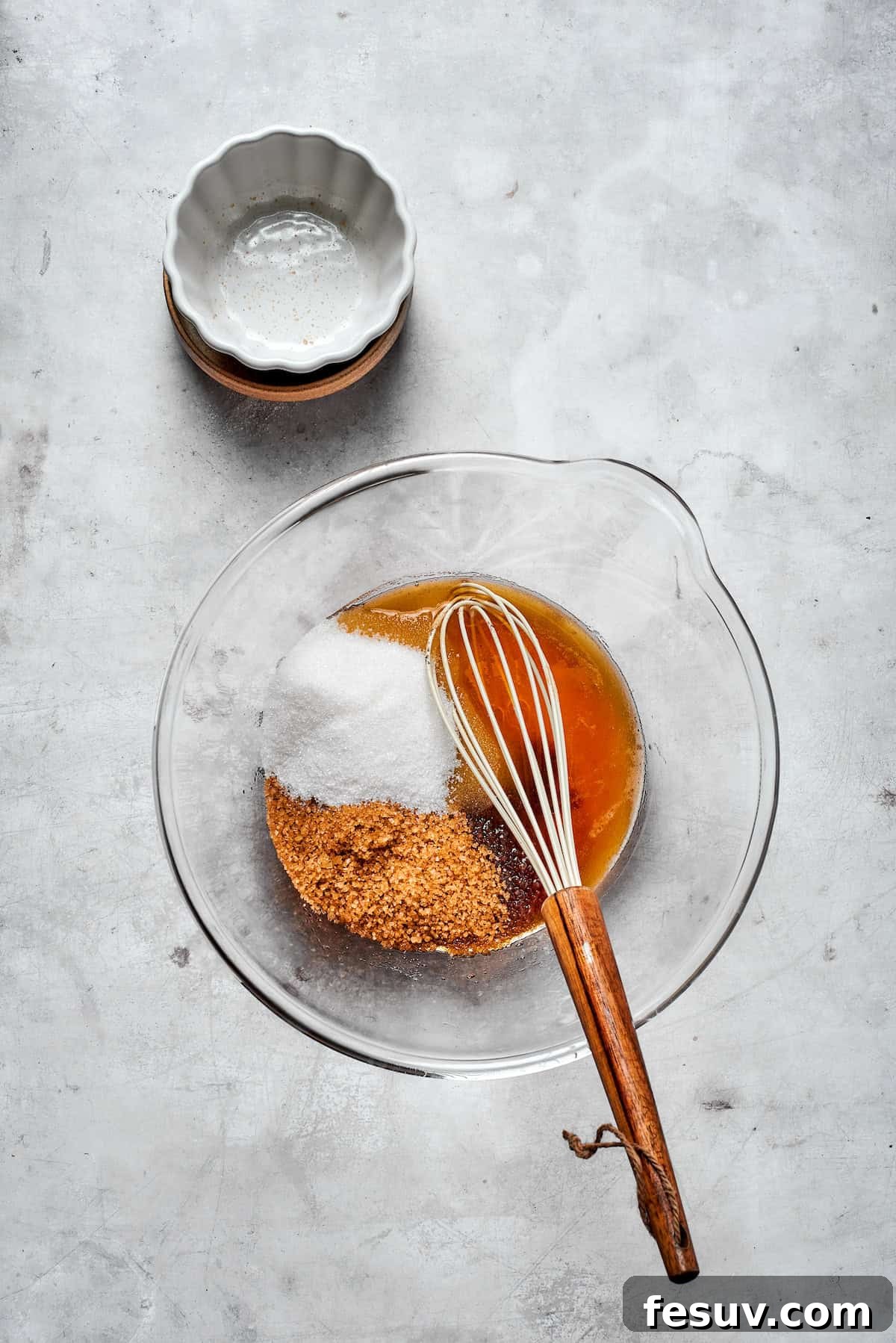White granulated sugar and dark brown sugar being whisked into a bowl of cooled brown butter.