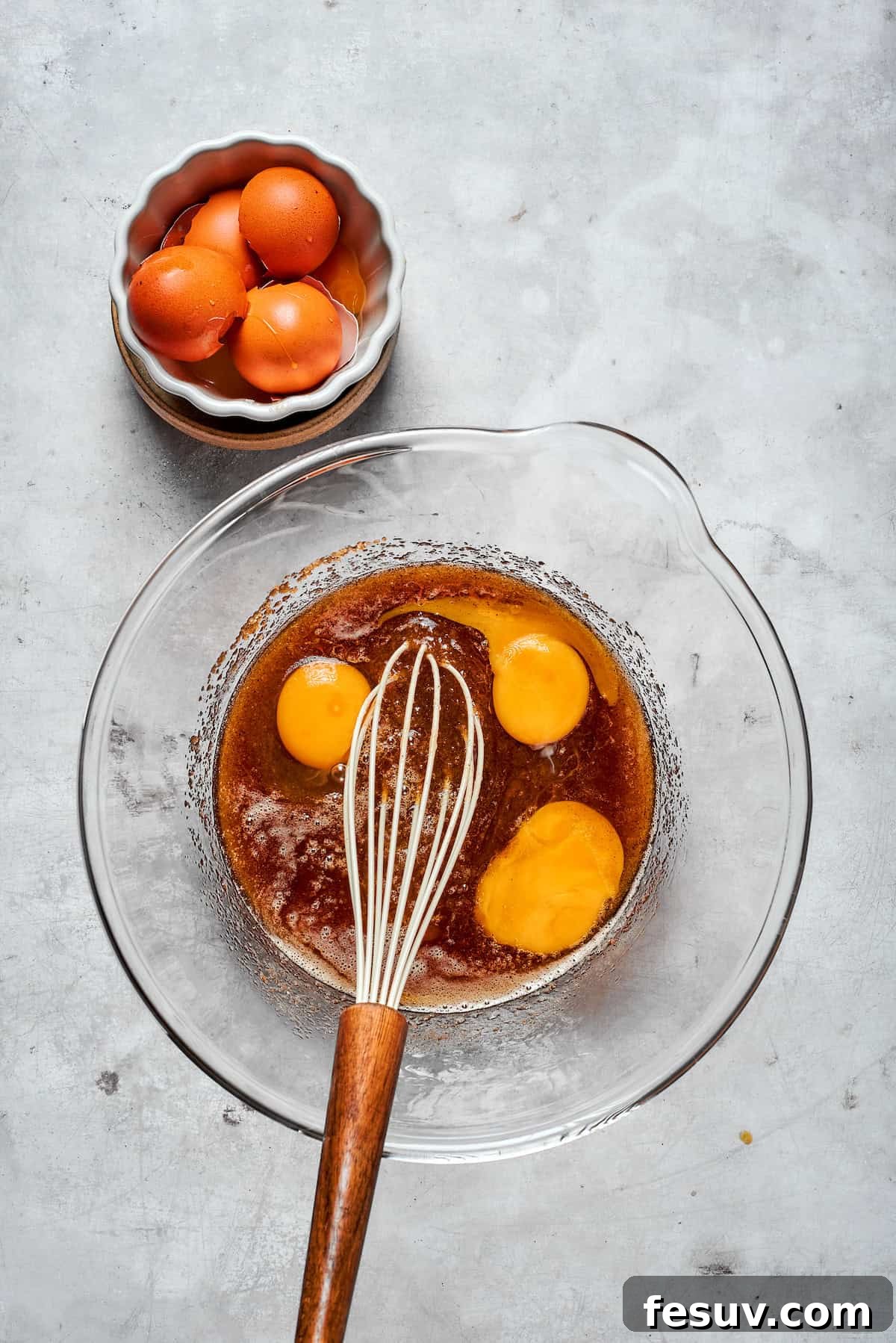 Two large eggs and one egg yolk added to the brown butter and sugar mixture in a mixing bowl.