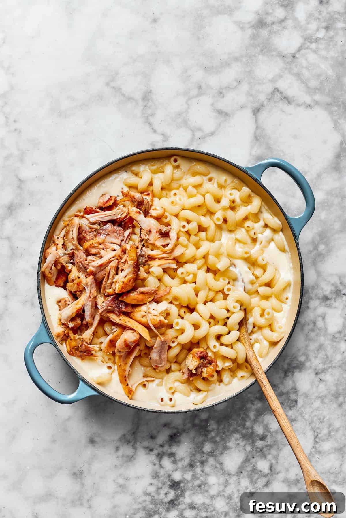 Combine the pasta and shredded chicken with the luscious creamy sauce. Cooked pasta noodles and flavorful shredded chicken being combined with the creamy garlic parmesan sauce in a large pan, ready to be tossed together for a complete dish.