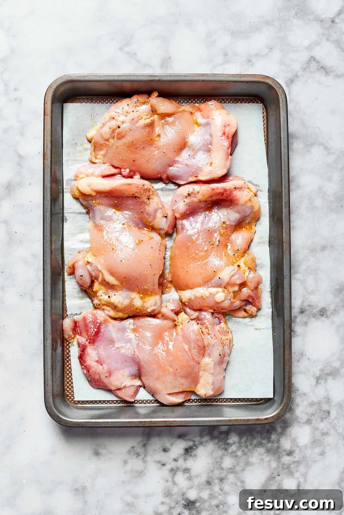 Season and arrange chicken for perfect roasting. Raw chicken thighs seasoned with salt, pepper, and garlic powder, arranged in a single layer on a baking sheet lined with parchment paper, anticipating roasting.