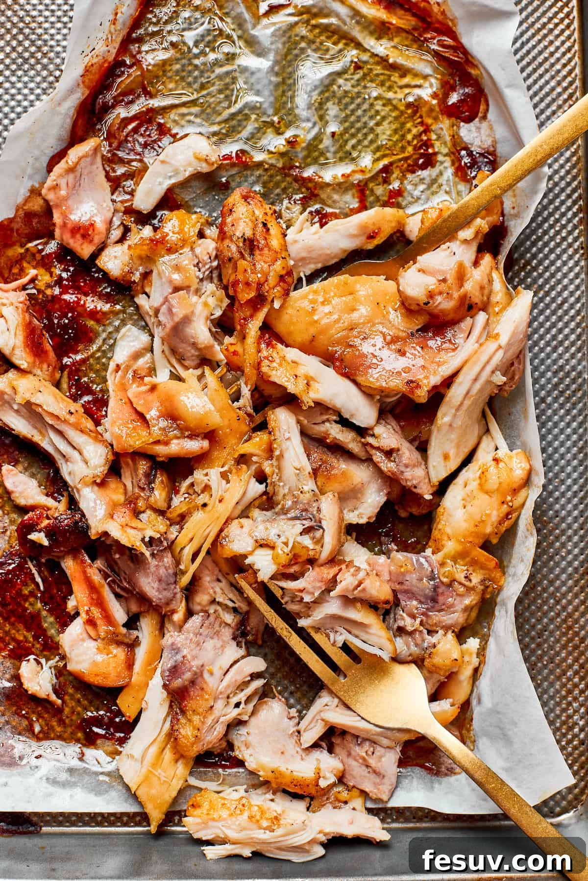 Succulent shredded cooked chicken, ideal for mixing with pasta. Perfectly cooked and tender shredded chicken pieces resting on a baking sheet after being roasted, ready to be folded into the creamy pasta.