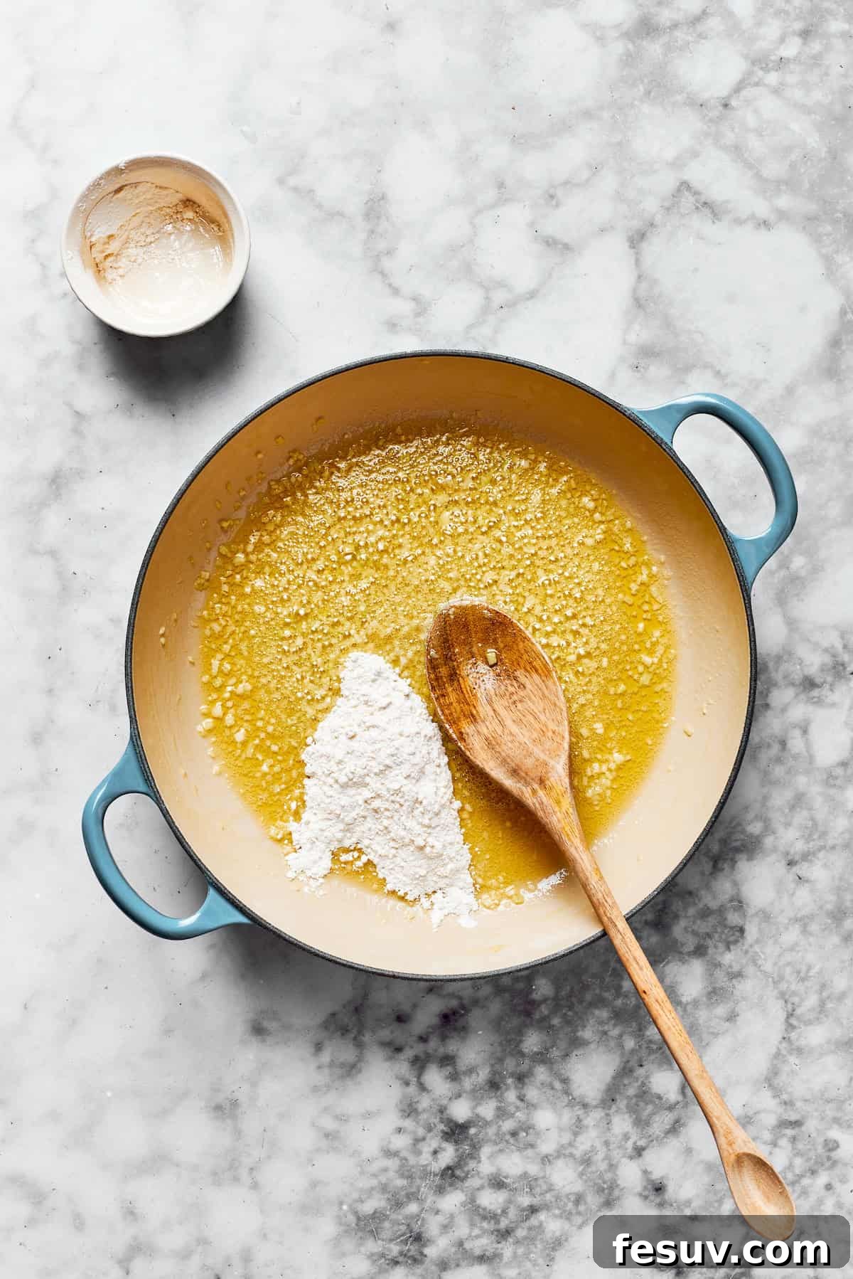 Sauté minced garlic, then create the essential roux with flour and butter. Melted butter and flour are whisked together vigorously in a large saucepan over medium heat, forming the base of a perfectly smooth roux for the creamy sauce.