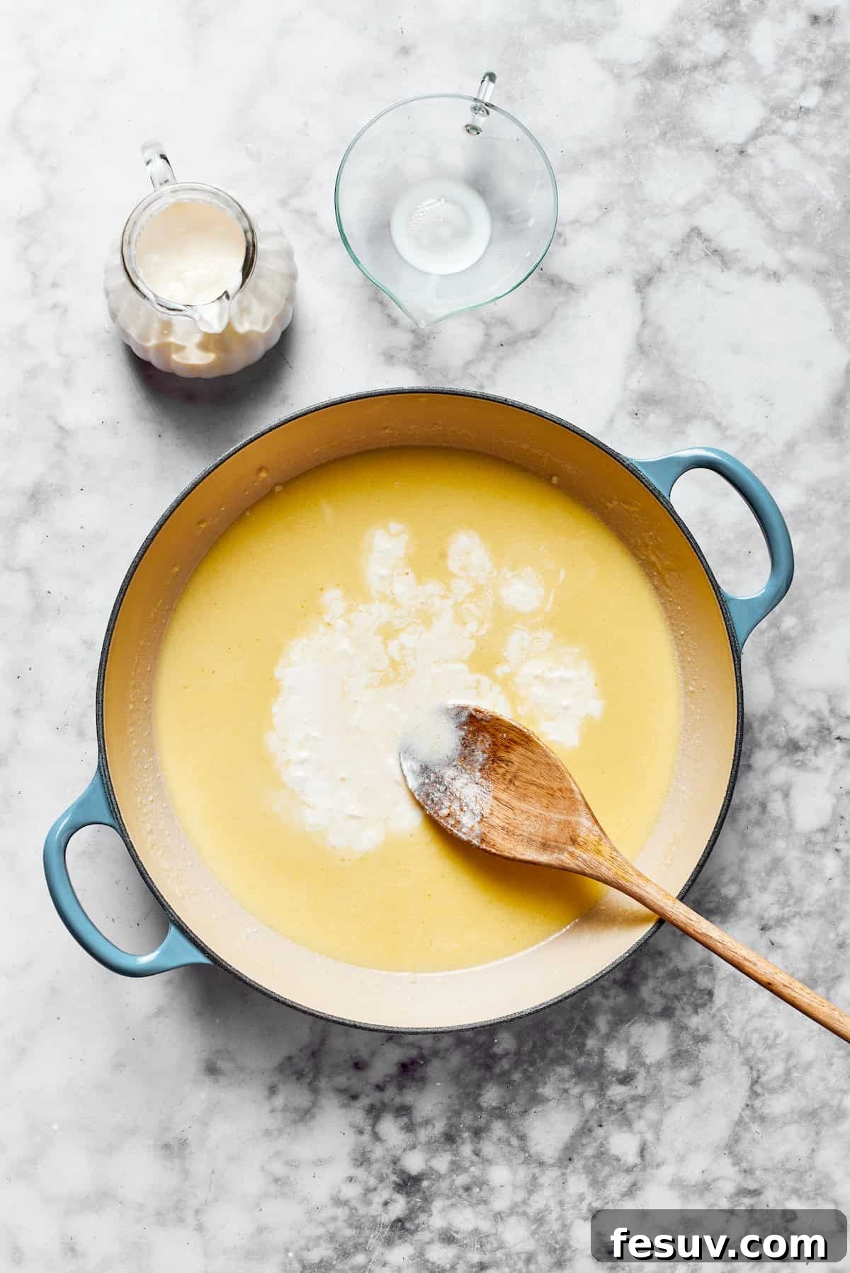Gradually add milk and then heavy cream to the thickening roux. Milk and heavy cream are gradually added to the rich roux in a saucepan, being whisked continuously to create a smooth, lump-free creamy sauce base.