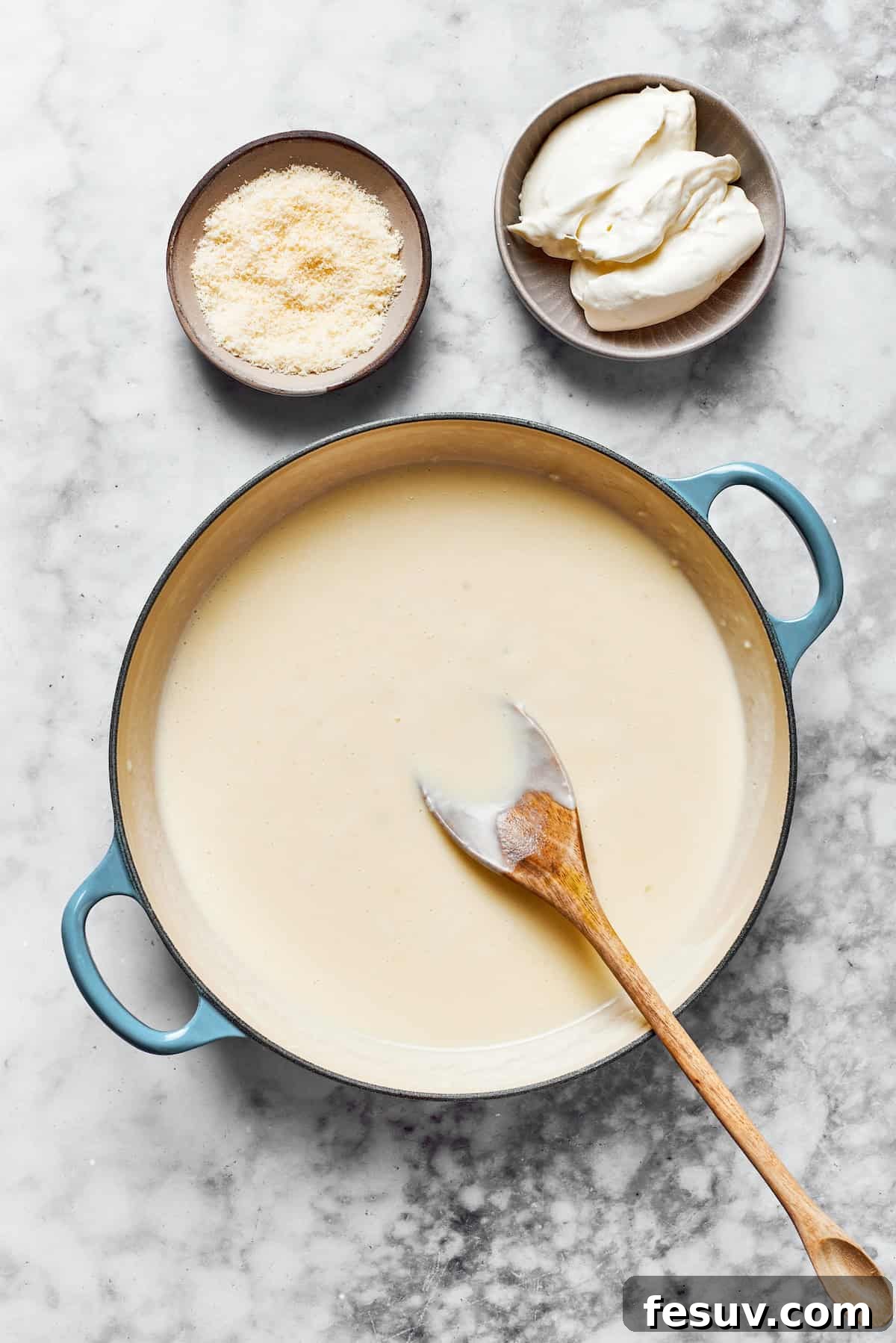 Whisk the sauce until it achieves a perfectly smooth and desired consistency. A creamy, beautifully thickened roux in a pan, smooth and ready for the cheeses, positioned next to bowls of freshly shredded Parmesan and perfectly cubed cream cheese.