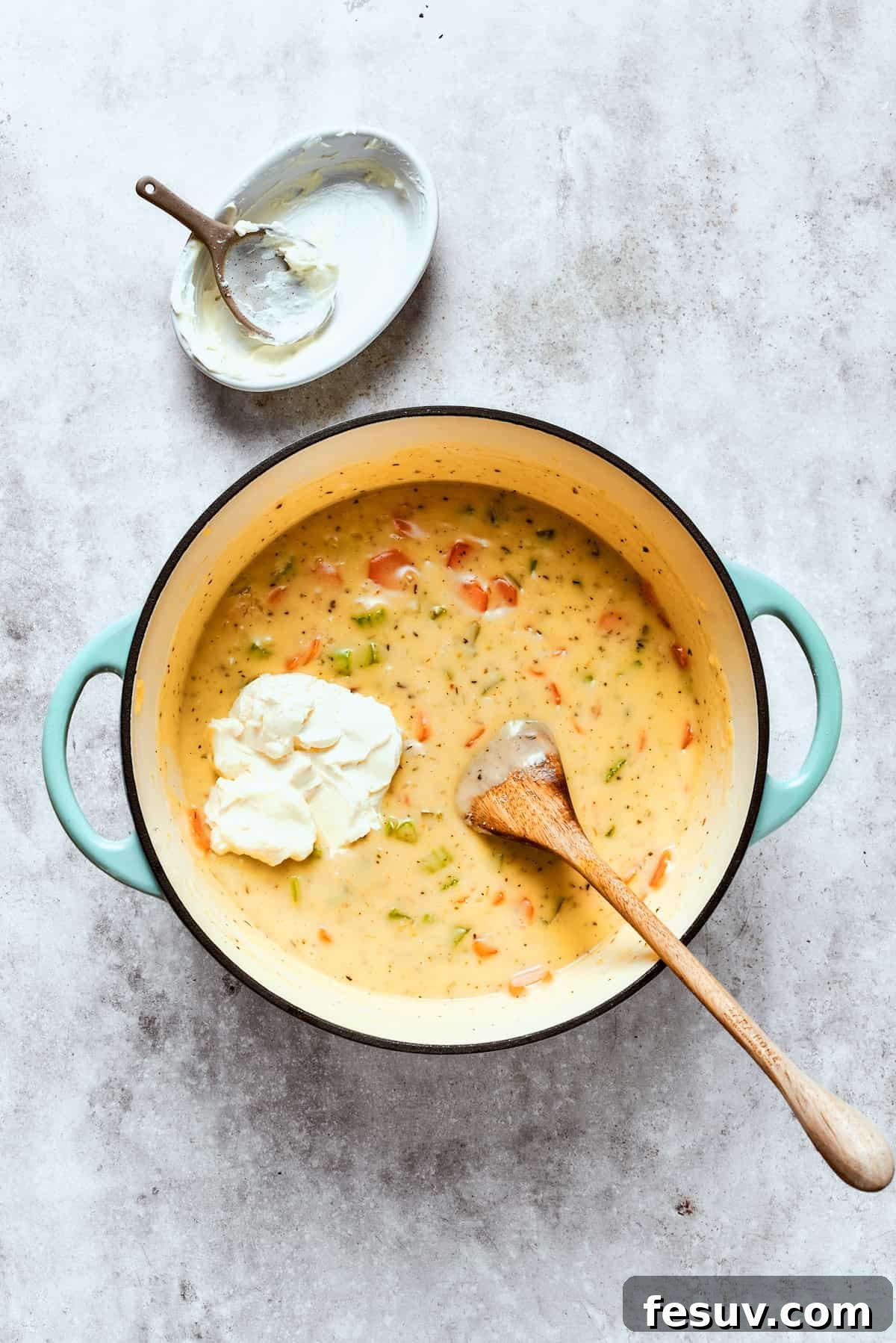 Chicken pot pie casserole is everything you love about the classic comfort food, baked under fluffy buttermilk biscuits instead of pie crust! Softened cream cheese being stirred into a large pot of chicken pot pie filling.