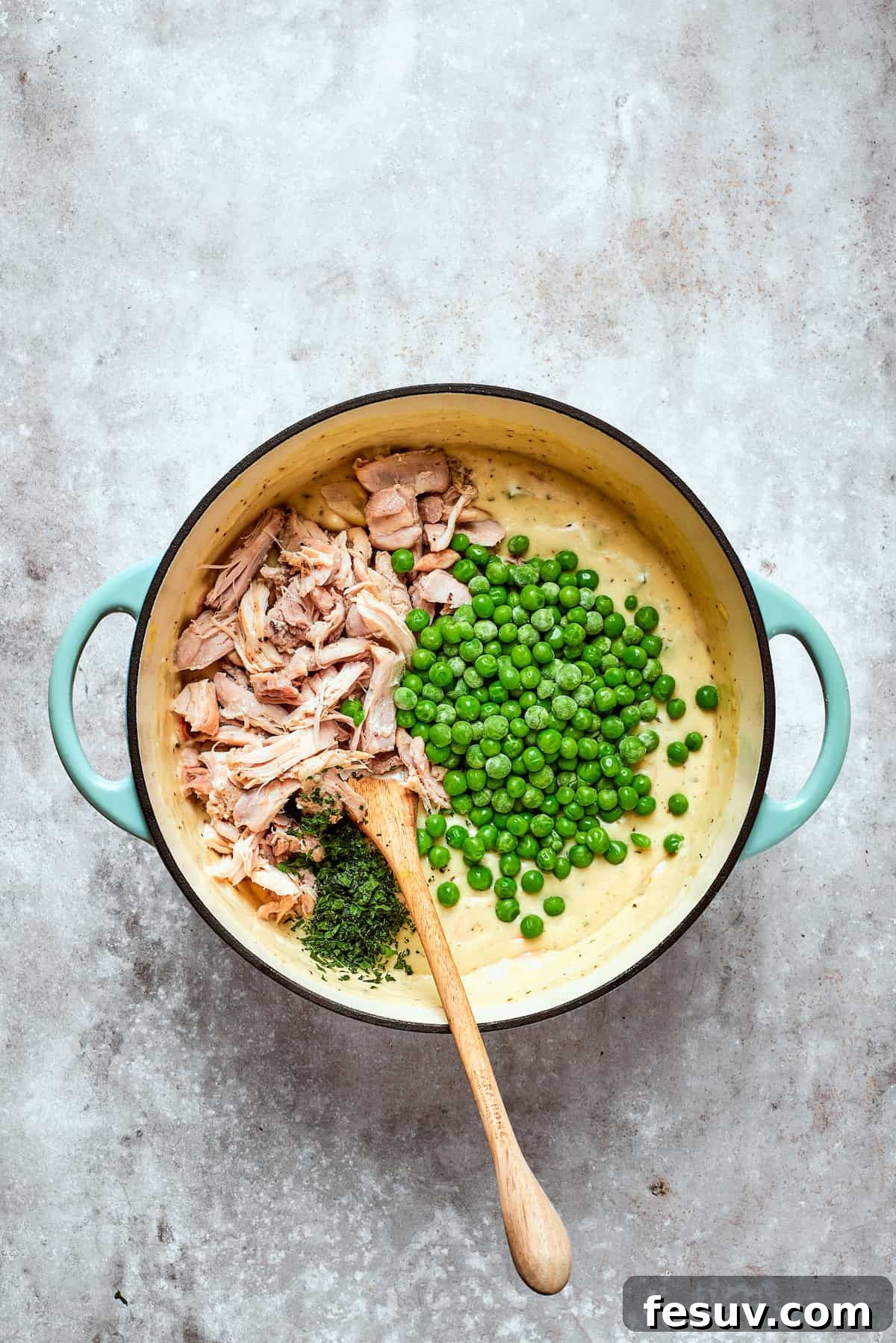 Chicken pot pie casserole is everything you love about the classic comfort food, baked under fluffy buttermilk biscuits instead of pie crust! Cooked shredded chicken and frozen peas being stirred into the creamy pot pie filling in a large pot.