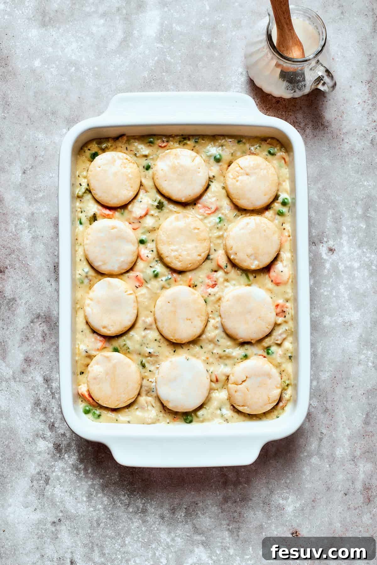 Chicken pot pie casserole is everything you love about the classic comfort food, baked under fluffy buttermilk biscuits instead of pie crust! A casserole dish filled with chicken pot pie filling, topped with raw biscuit circles, ready to be baked.