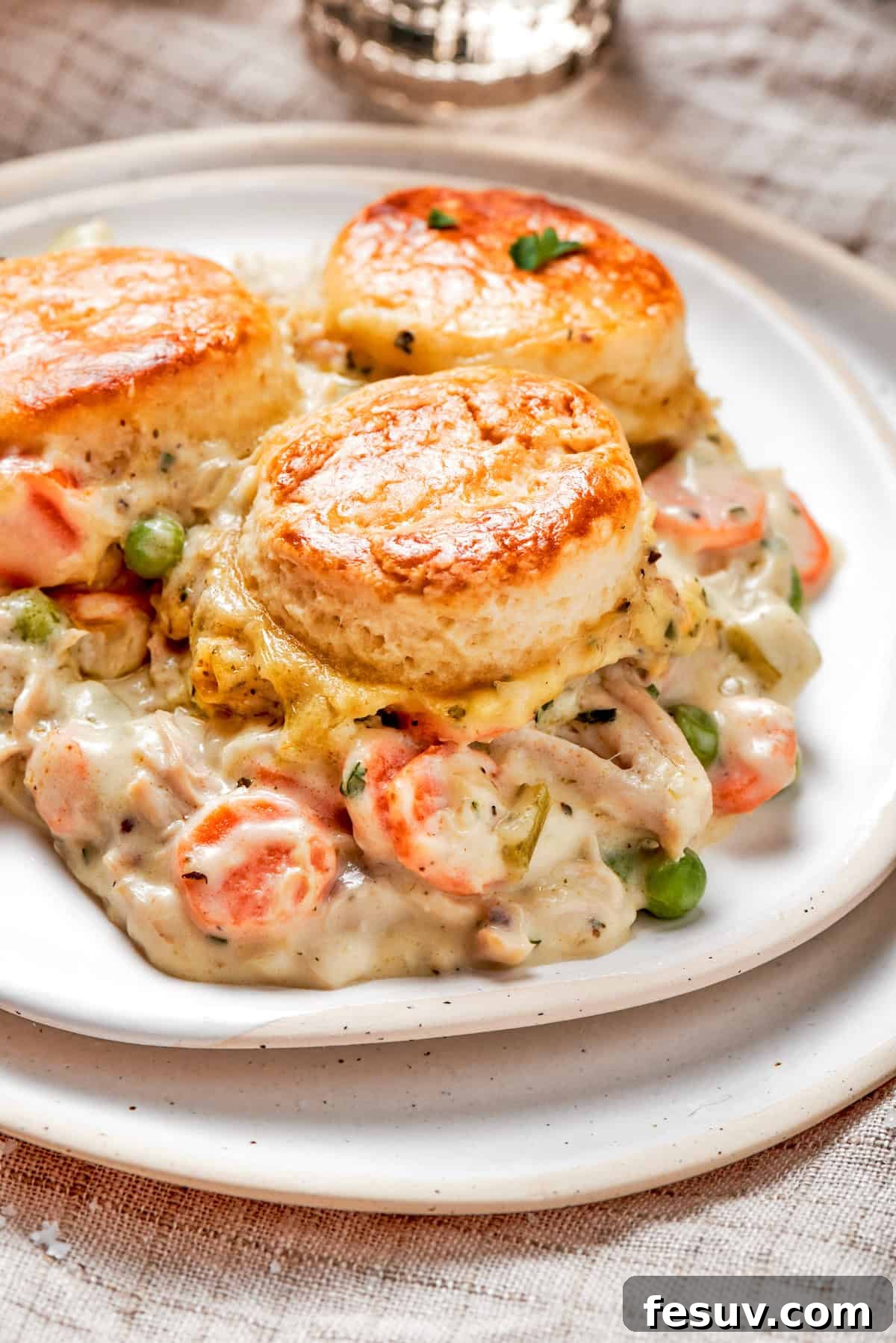 Chicken pot pie casserole is everything you love about the classic comfort food, baked under fluffy buttermilk biscuits instead of pie crust! A generous serving of chicken pot pie casserole on a white plate, showcasing the creamy filling and flaky biscuit topping.