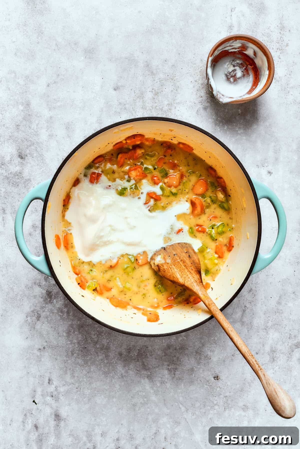 Chicken pot pie casserole is everything you love about the classic comfort food, baked under fluffy buttermilk biscuits instead of pie crust! Half-and-half being poured into a large pot containing the simmering chicken pot pie filling.