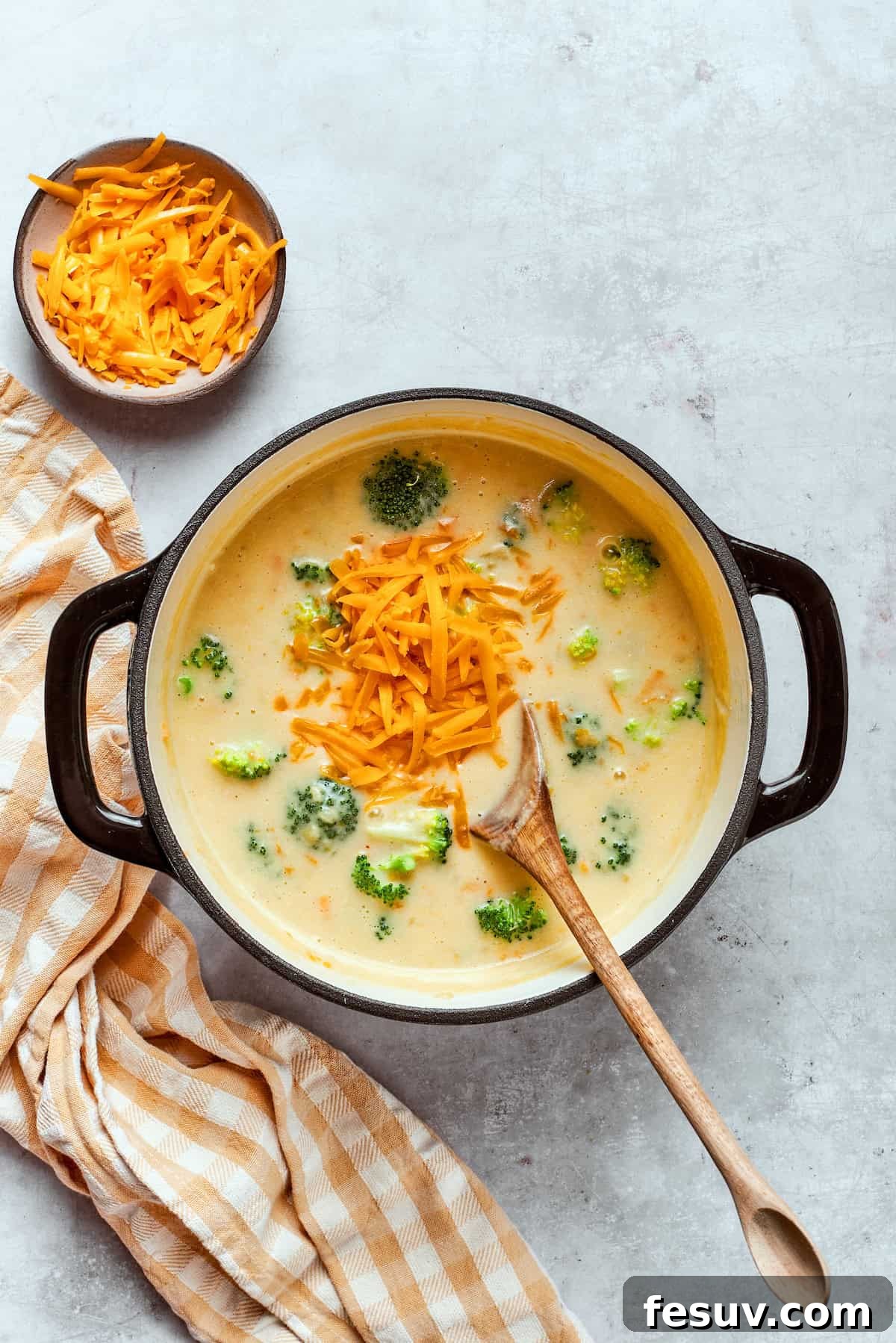 Adding shredded cheddar to a pot with soup.