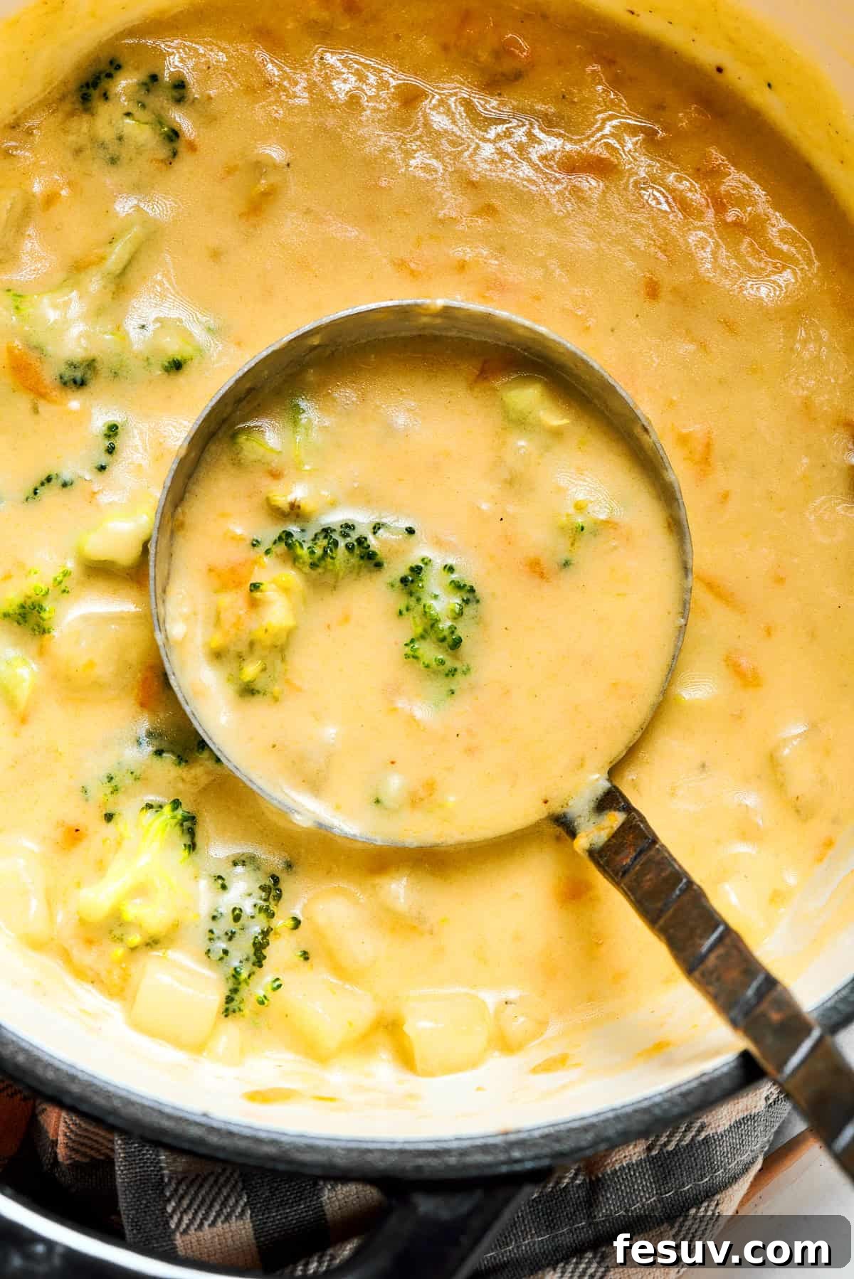 A ladle spooning out broccoli cheese soup from a cooking pot.