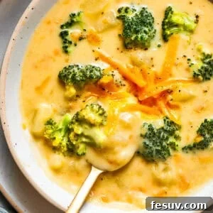 Bowl of broccoli cheese soup garnished with shredded cheese and broccoli florets.