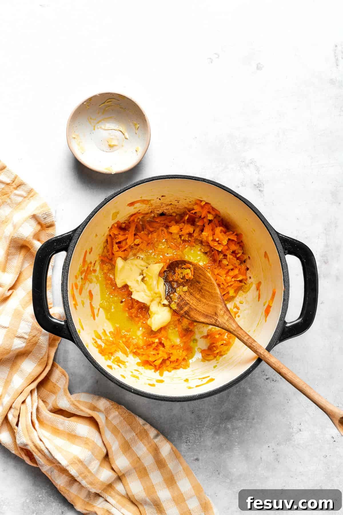 Adding butter to a pot with shredded carrots.