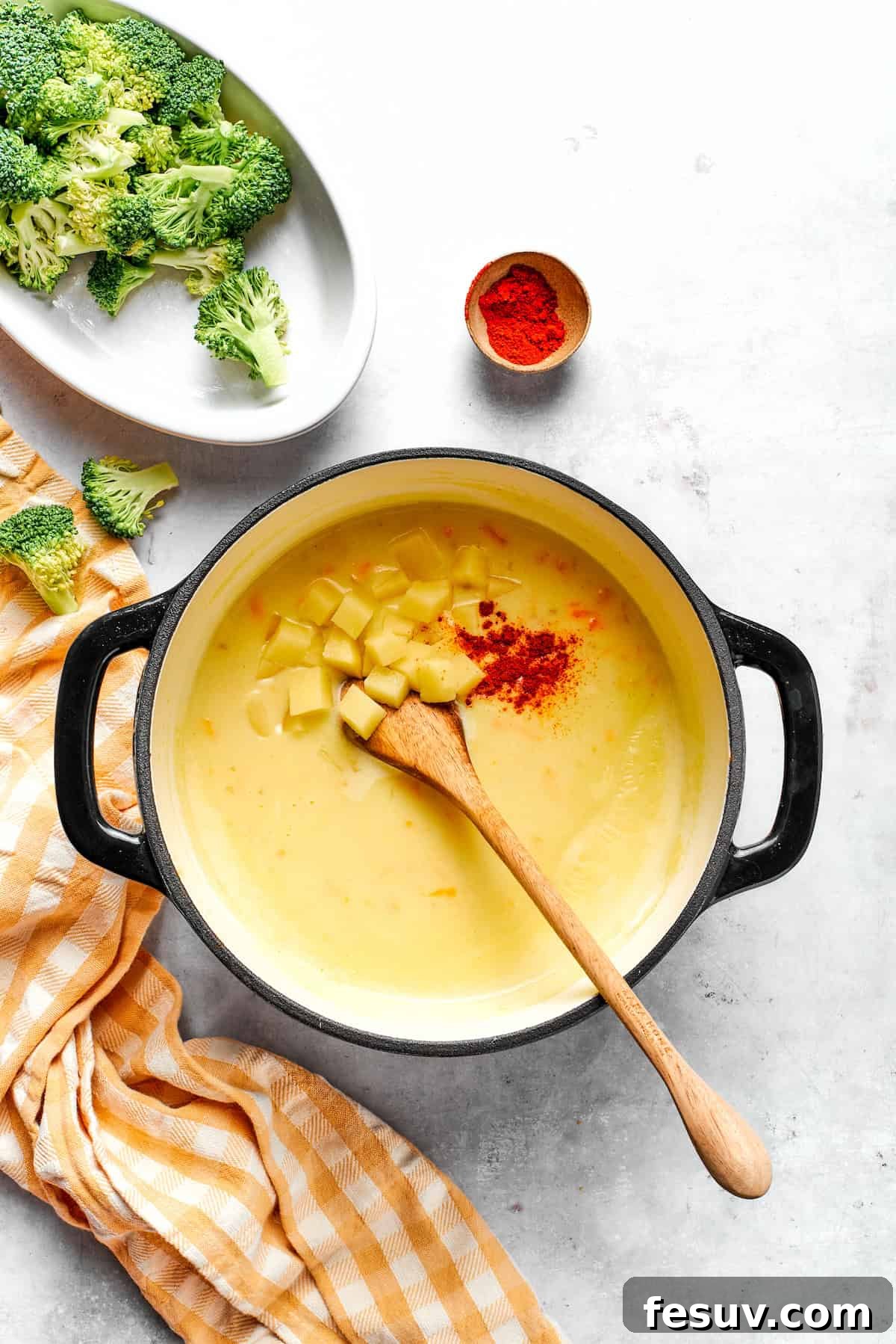 Adding diced potato and paprika to soup in a pot.