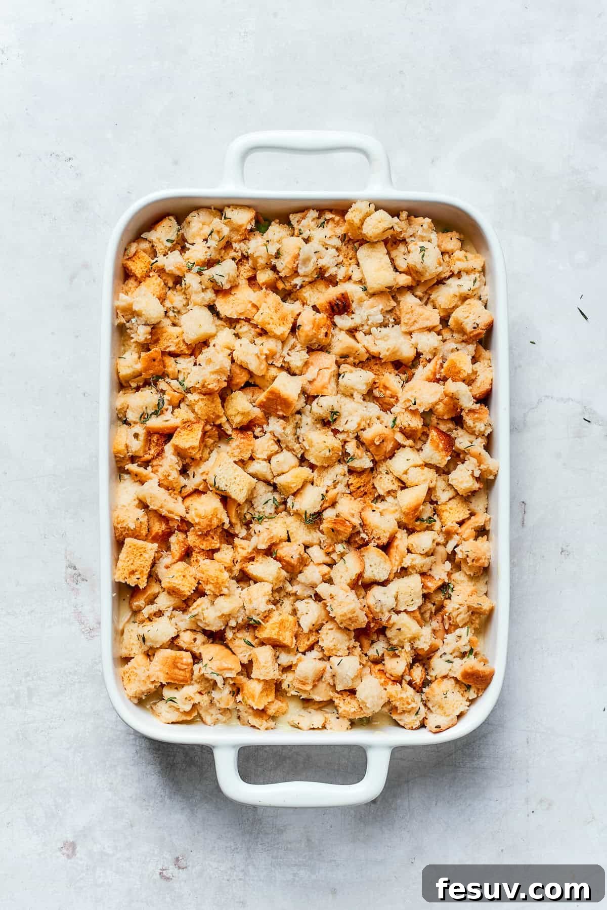 A layer of stuffing being spread over the chicken filling in a baking dish.