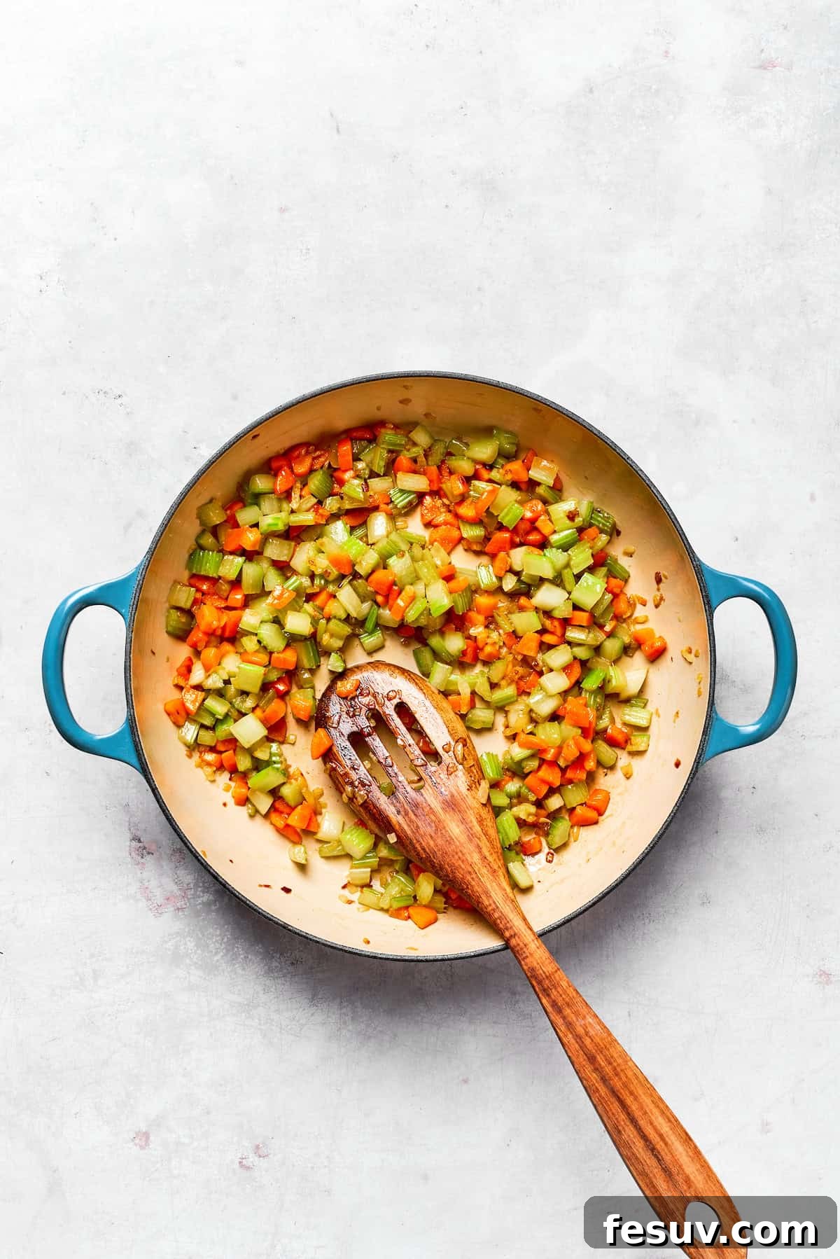 Cooked onions, carrots, and celery looking tender in a pot.